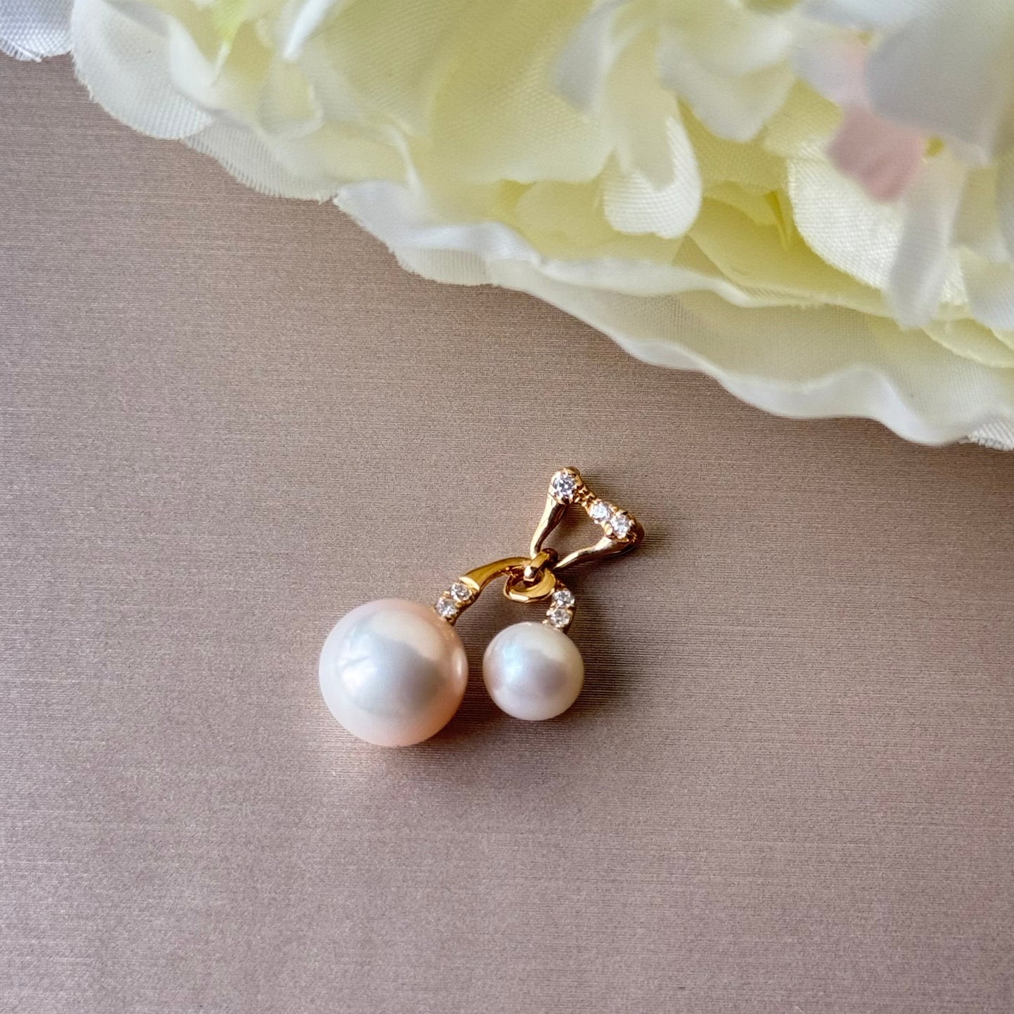 Pearl pendant with gold accents on a beige surface with a light pink flower in the background.