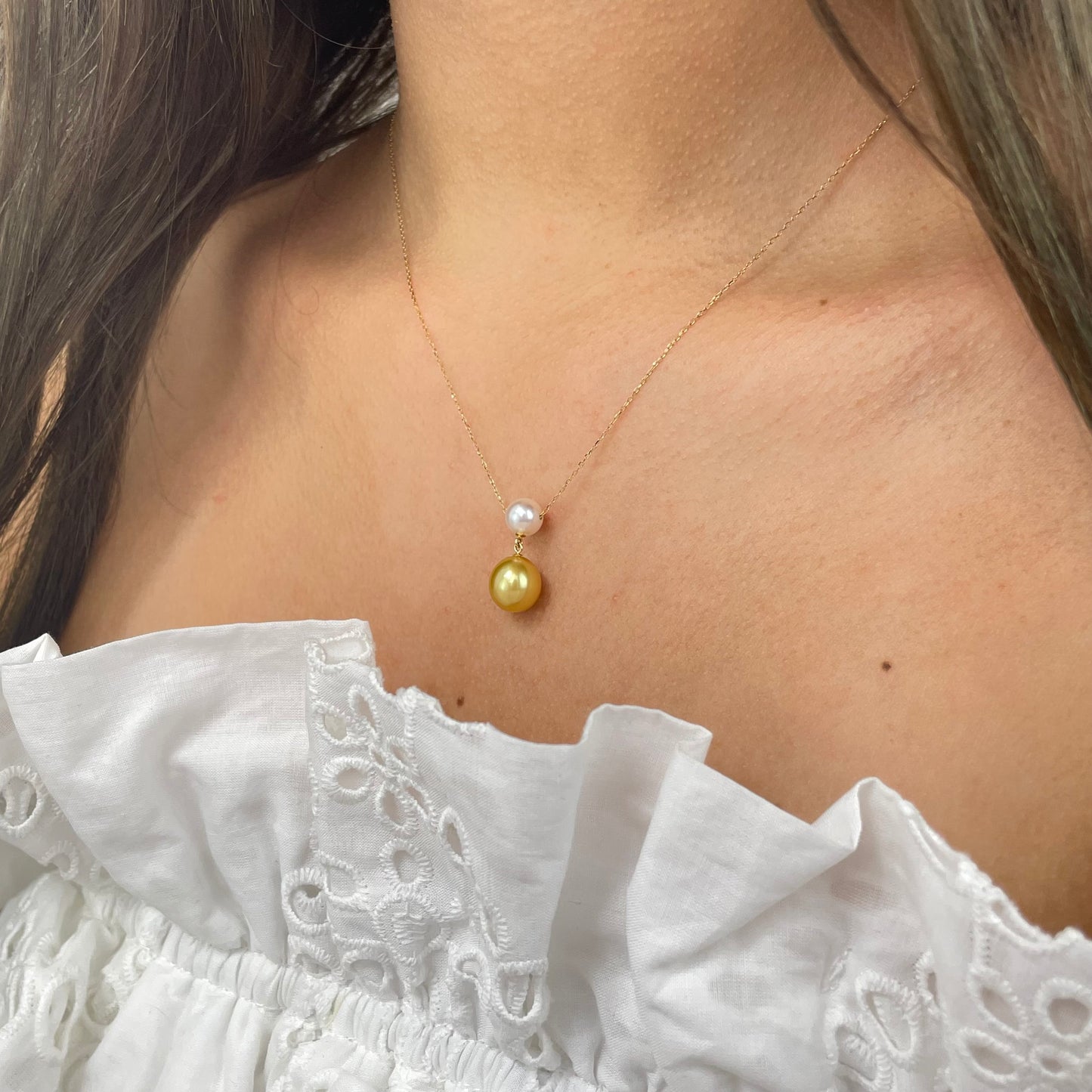 Gold necklace with a gold and white pearl on a person wearing a white top.