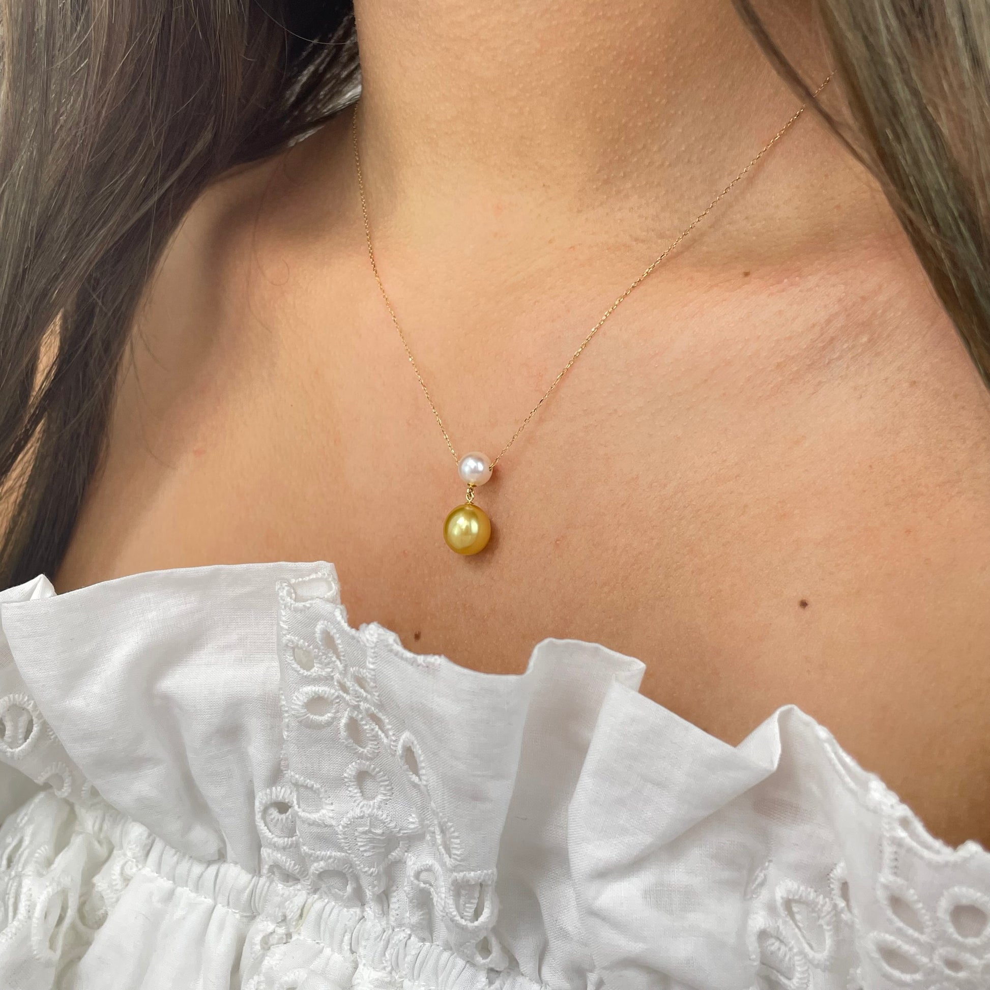Gold necklace with a gold and white pearl on a person wearing a white top.