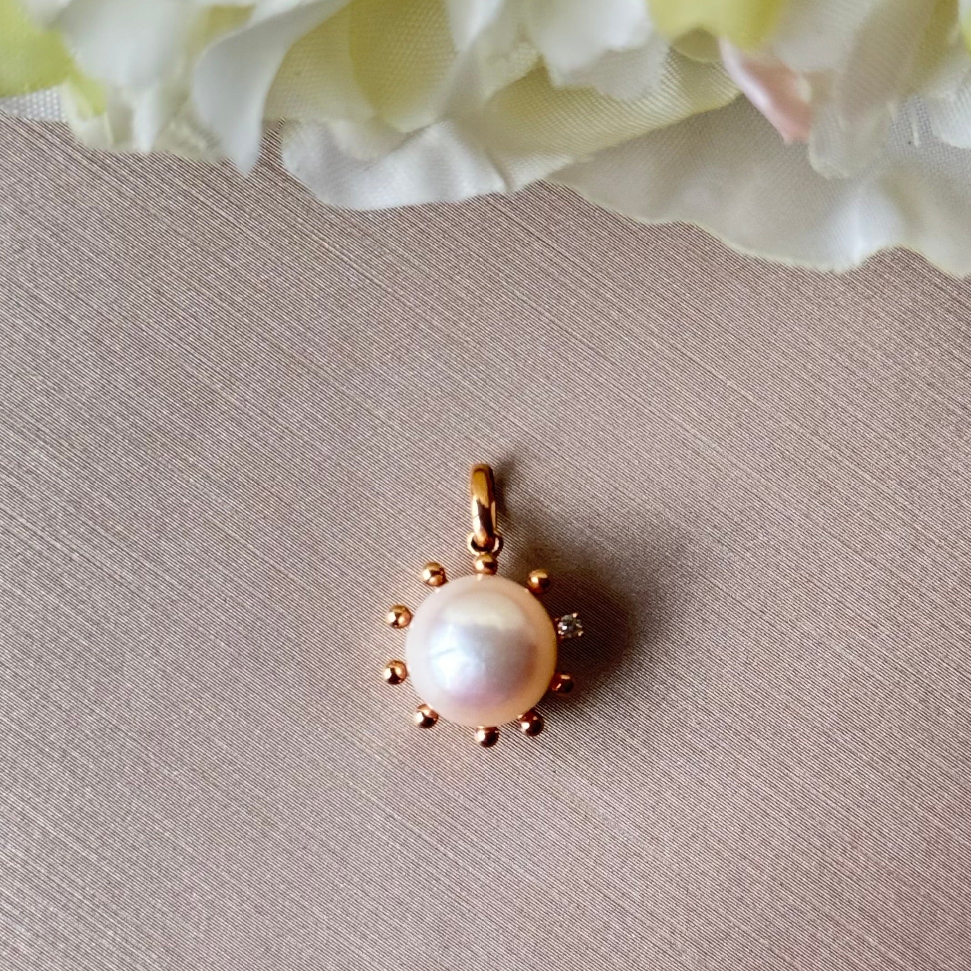 Pearl pendant with gold setting on a textured surface with flowers in the background.