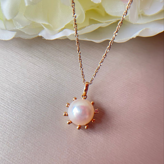 Pearl necklace with gold setting on a light pink surface with flowers in the background.