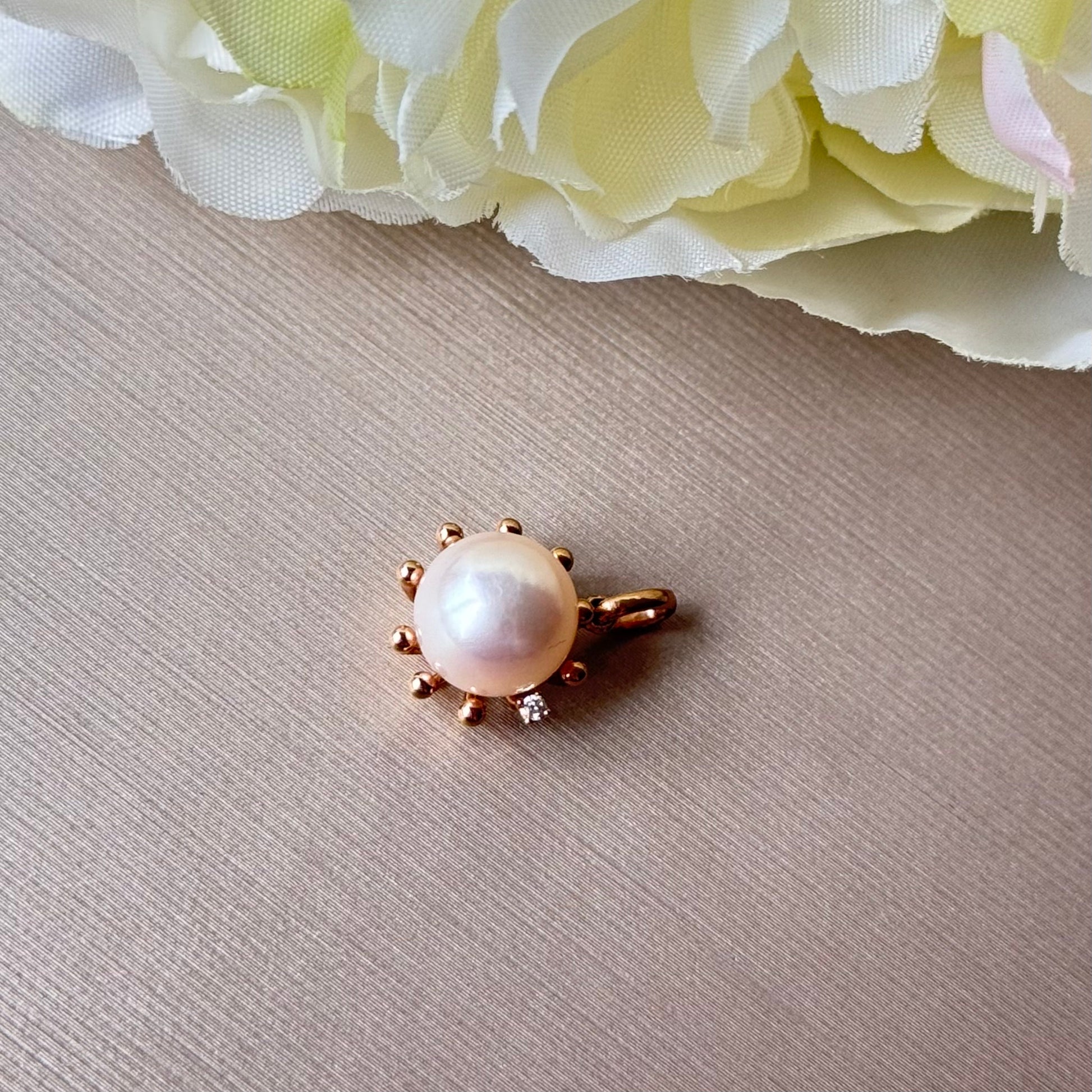 Akoya Pearl with gold setting on a brown surface with flowers in the corner.