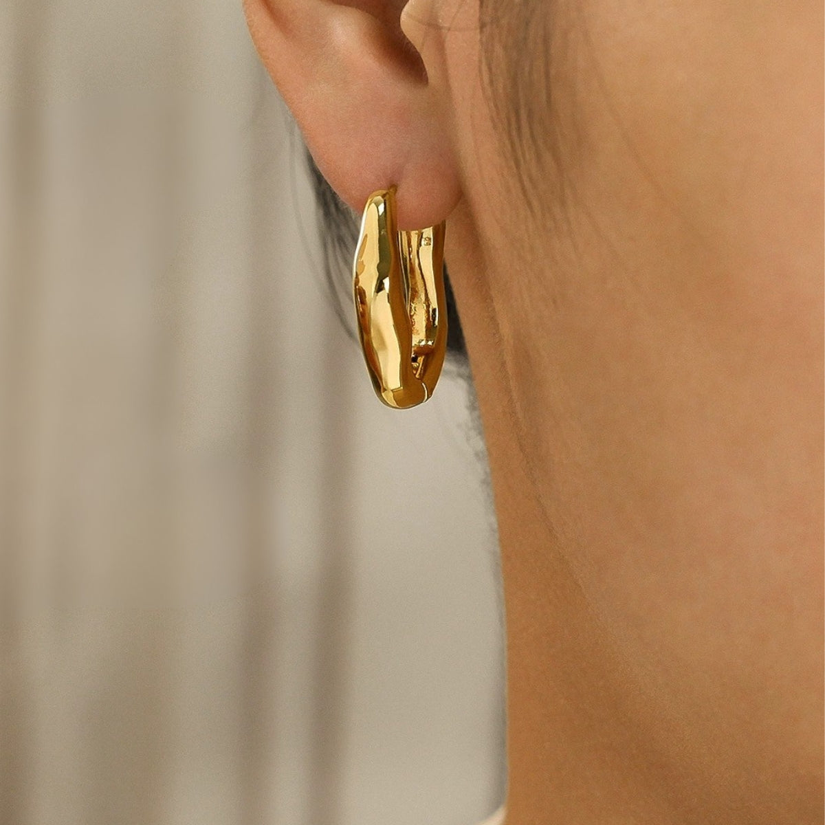 Gold hoop earring from SKADIS Jewelry worn by a person with a neutral background