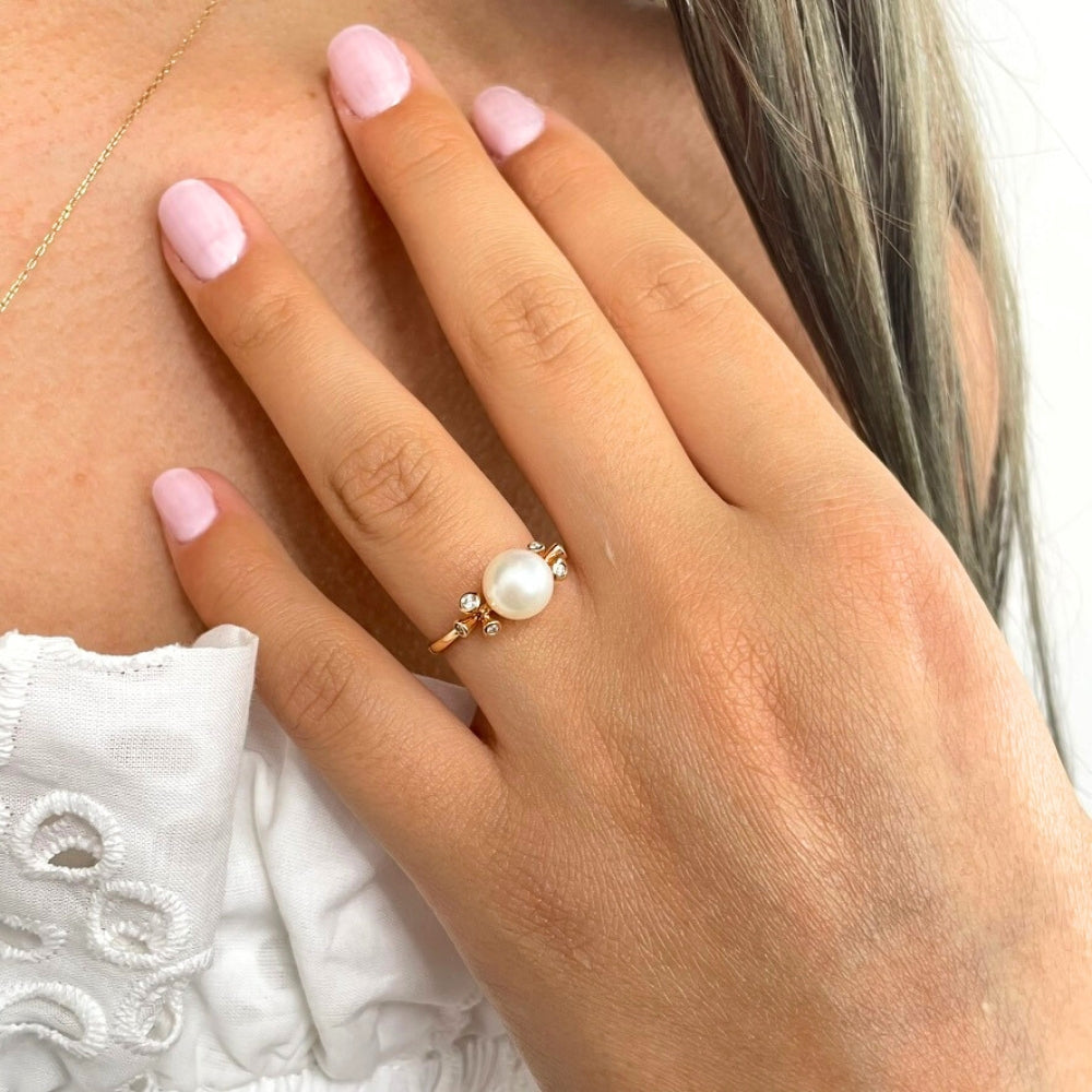 Akoya pearl ring in 18k gold with diamonds on a person's hand.