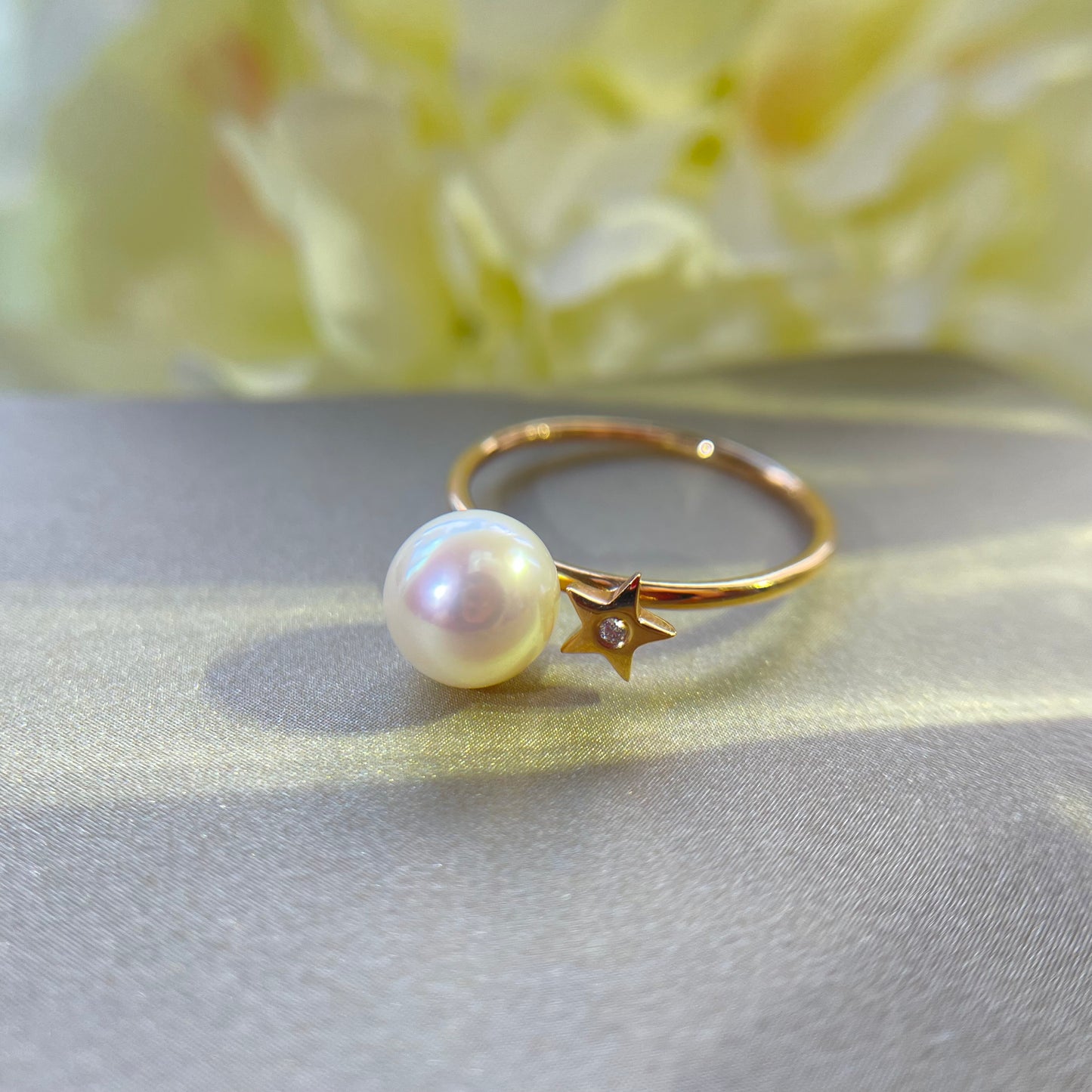 Gold ring with Akoya pearl and diamond on gold surface with a yellow floral background