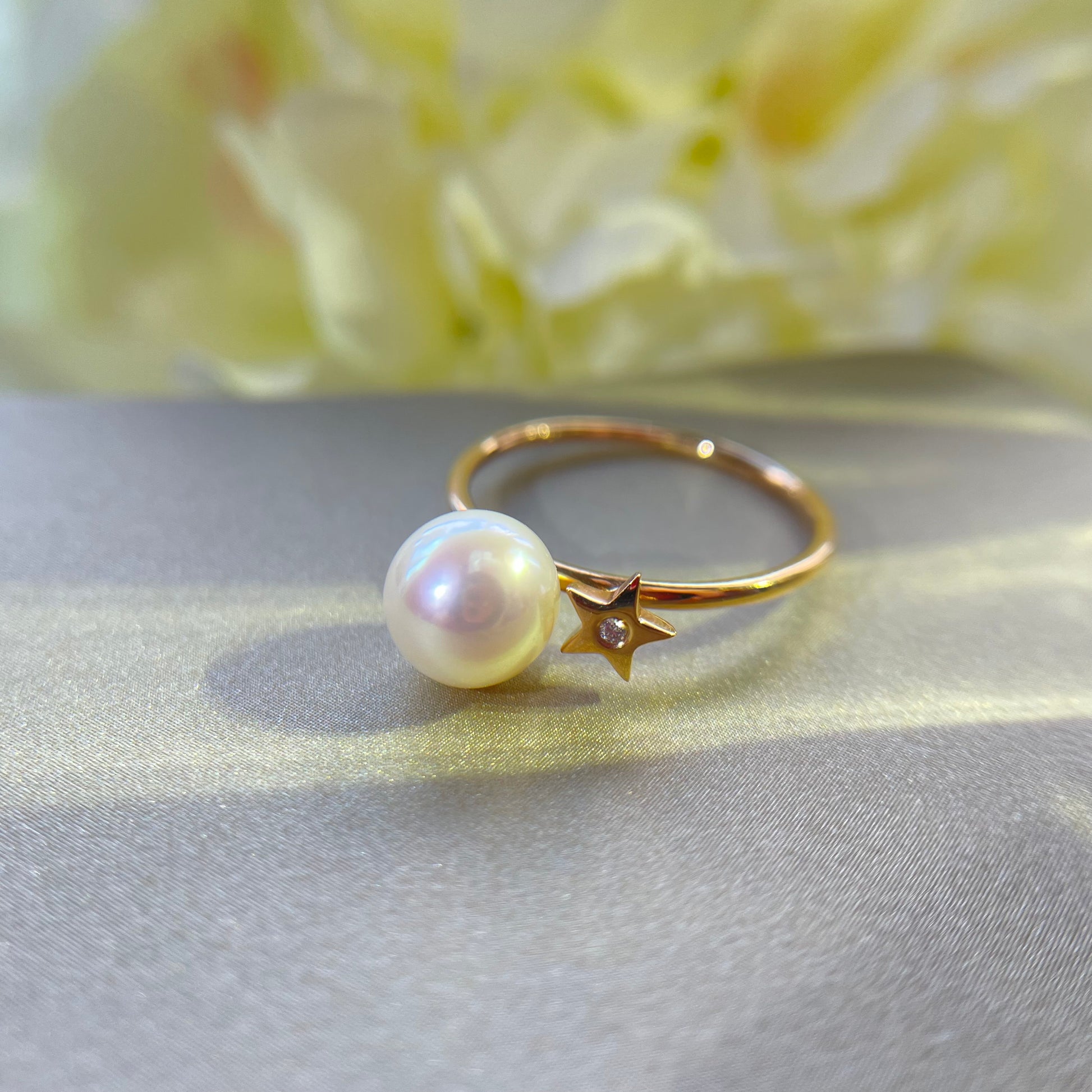 Gold ring with Akoya pearl and diamond on gold surface with a yellow floral background
