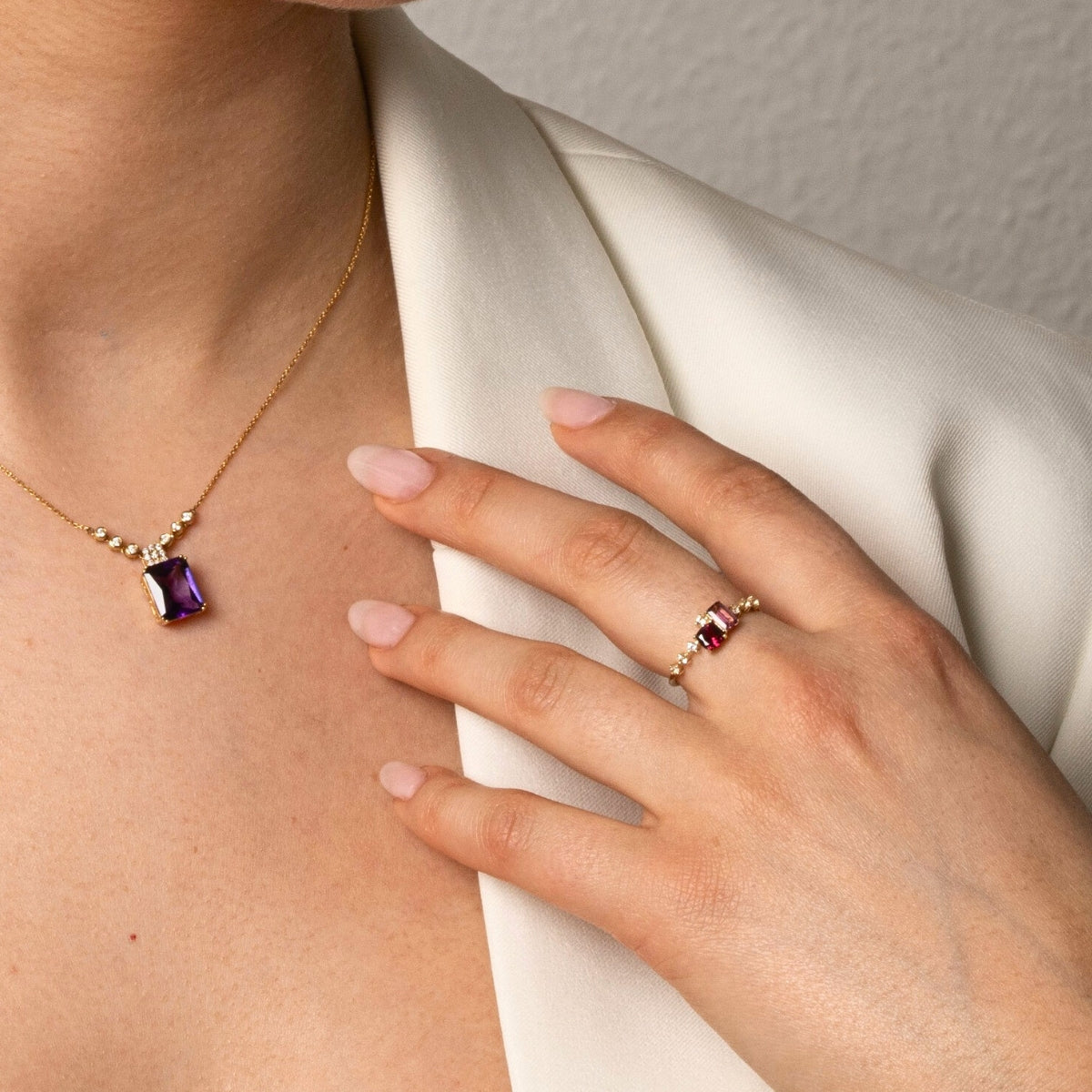 A person wearing Amethyst diamond necklace and a garnet gold ring with white jacket
