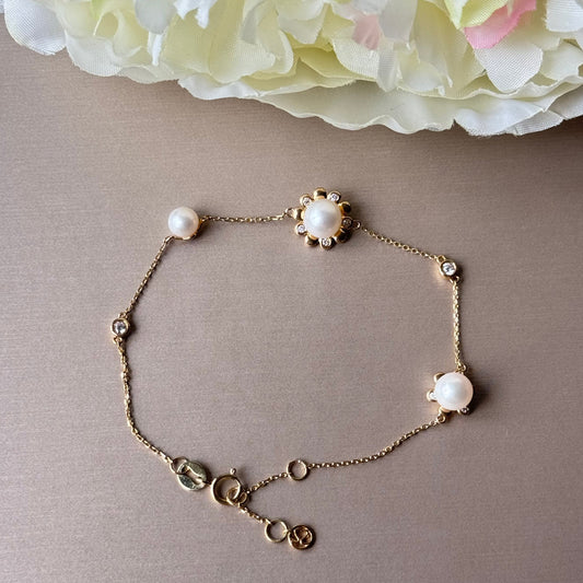Gold bracelet with pearls on a beige surface with white flowers in the background.