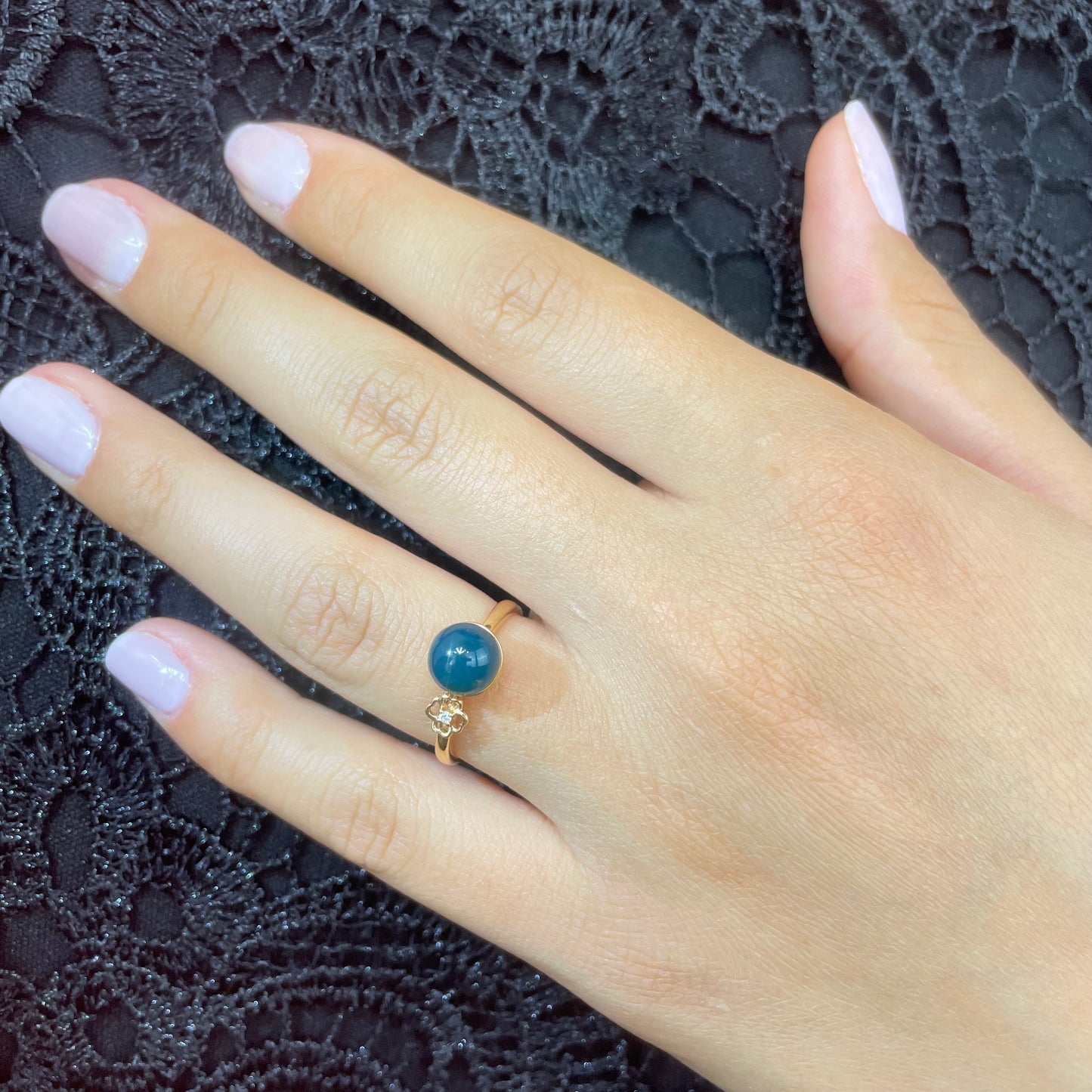 Close-up of a hand wearing a gold ring featuring a round blue amber gemstone and natural diamond.