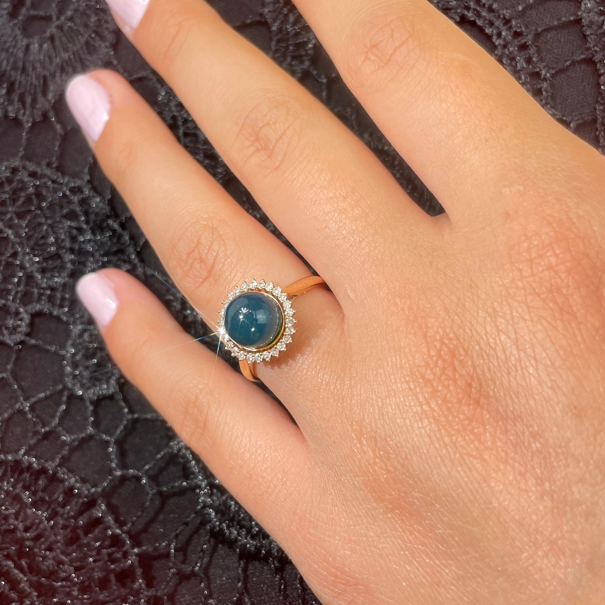 Hand wearing a ring with a blue amber gemstone and diamonds on a black background.