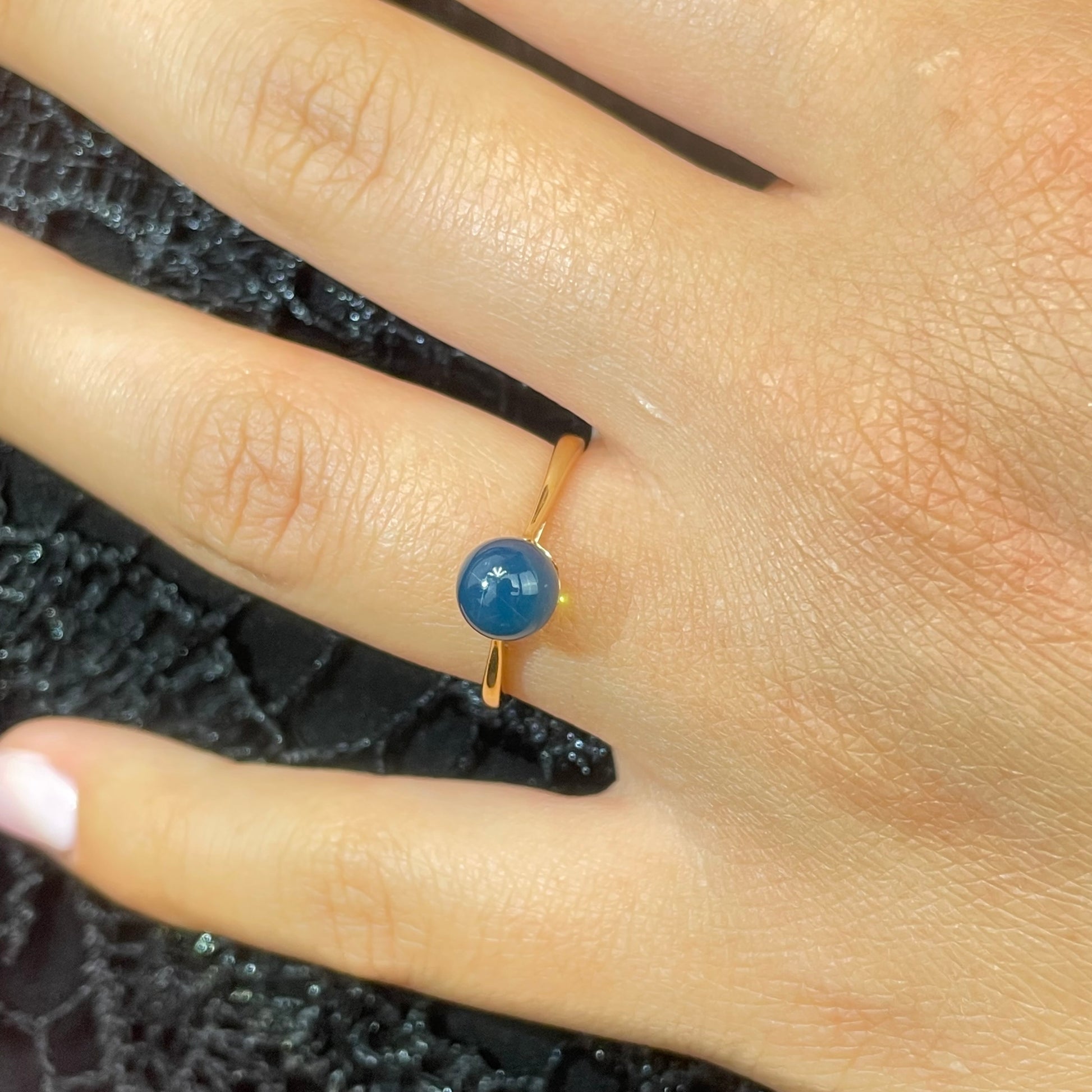 Gold ring with a blue amber gemstone on a finger against a textured black background