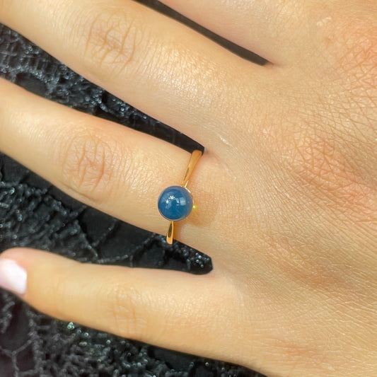 Gold ring with a blue amber gemstone on a finger against a textured black background