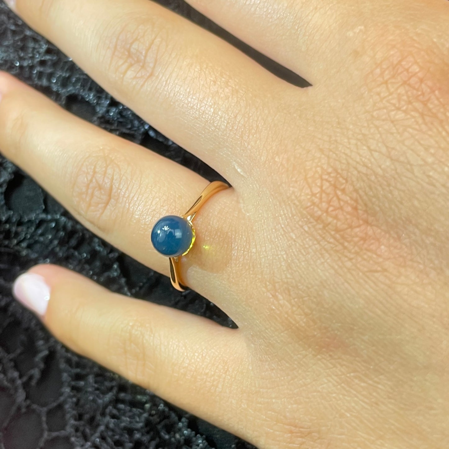Gold ring with a blue amber gemstone on a hand against a textured black background