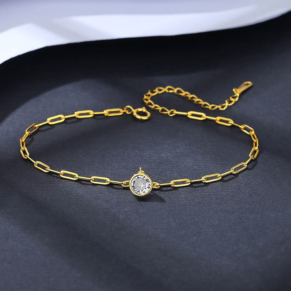Gold chain bracelet with a central zirconia on a dark fabric background