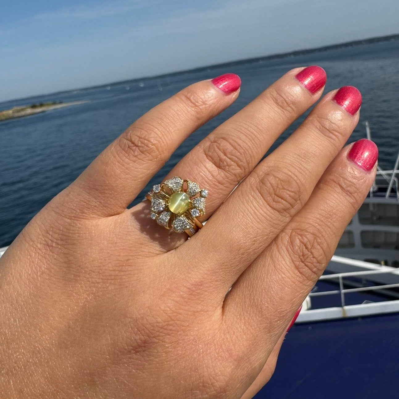 Hand wearing a ring with a cat's eye gemstone against a scenic background of water and sky.