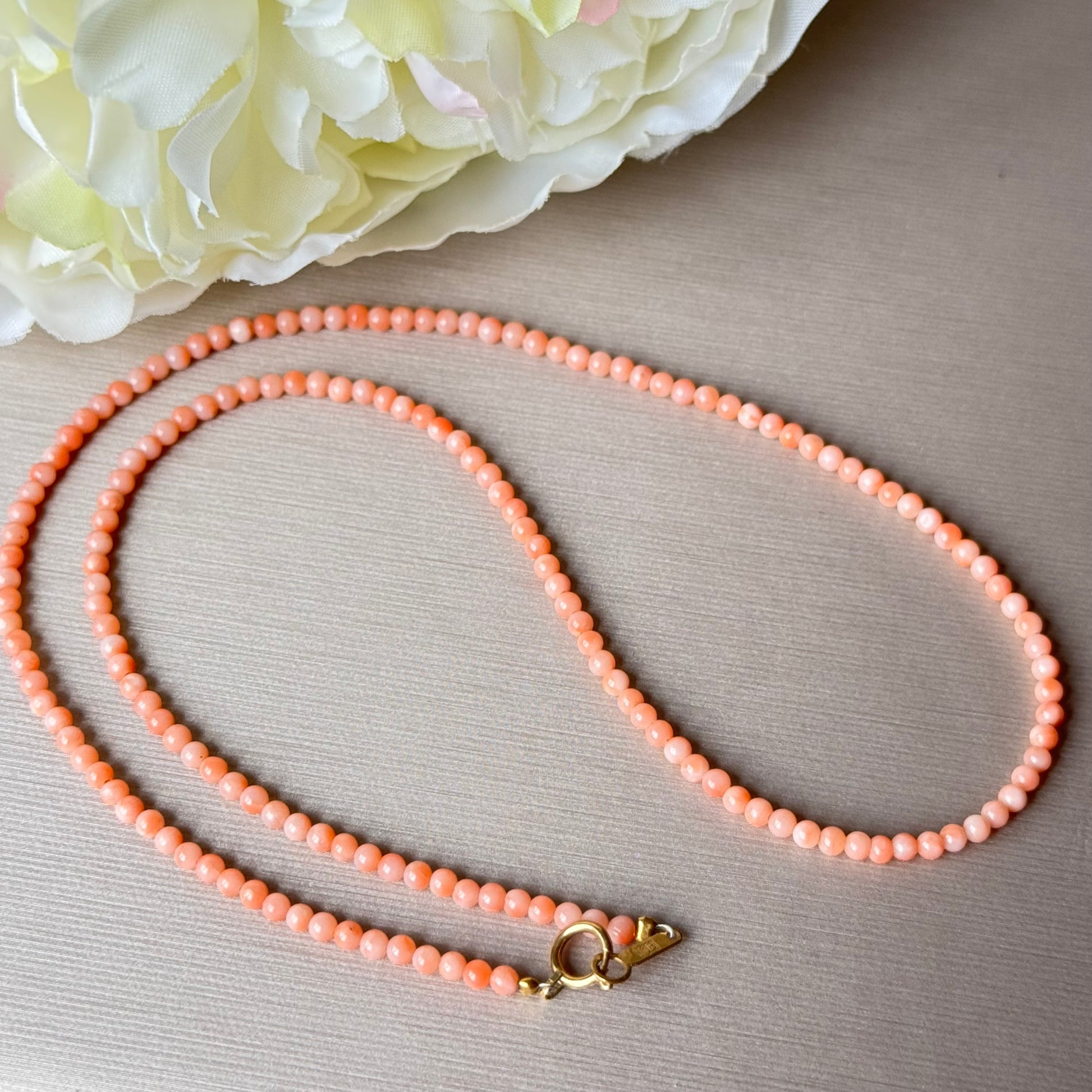 Peach-colored coral necklace with a gold clasp on a light gray surface with white flowers.