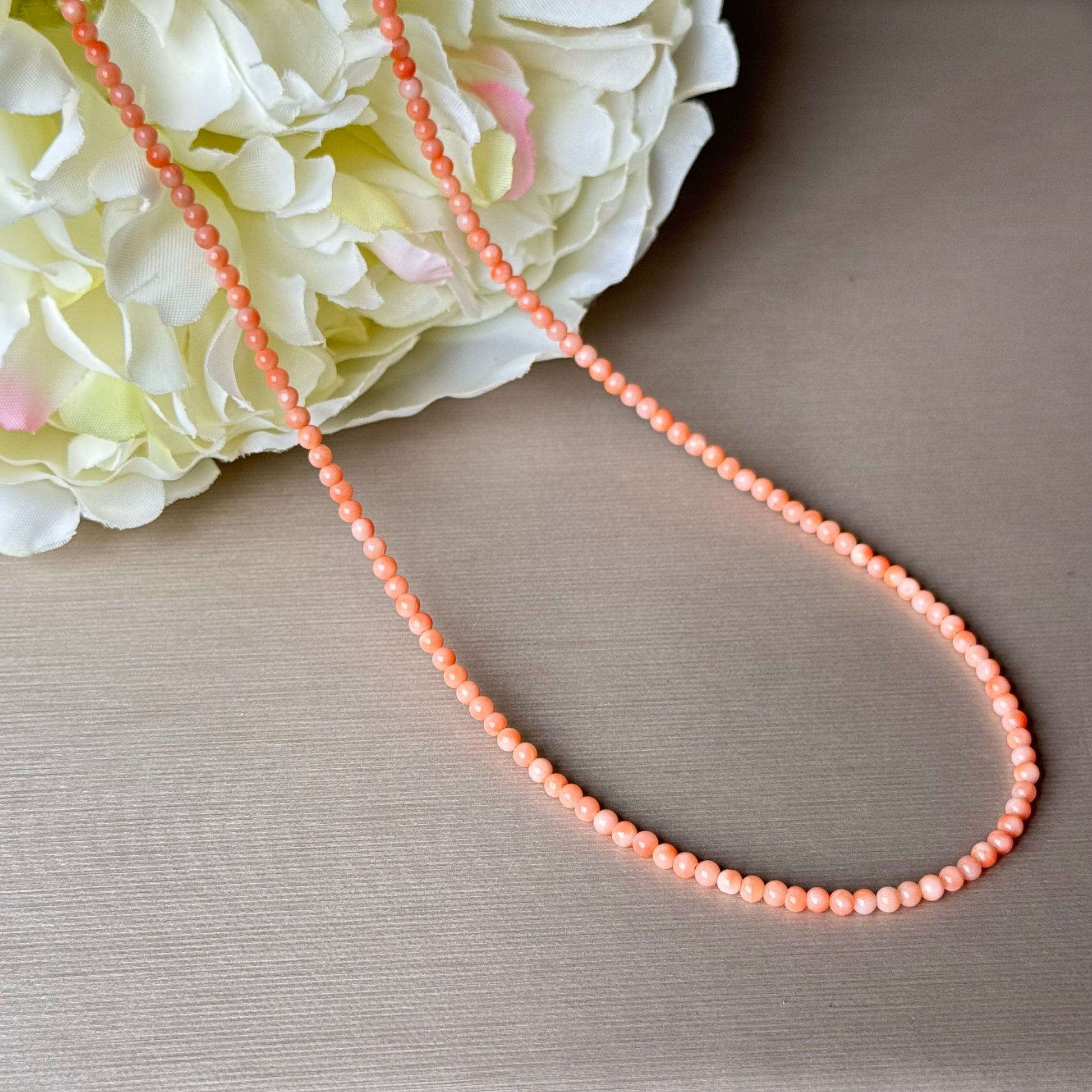 Peach-colored coral beaded necklace on a textured surface with a floral background.