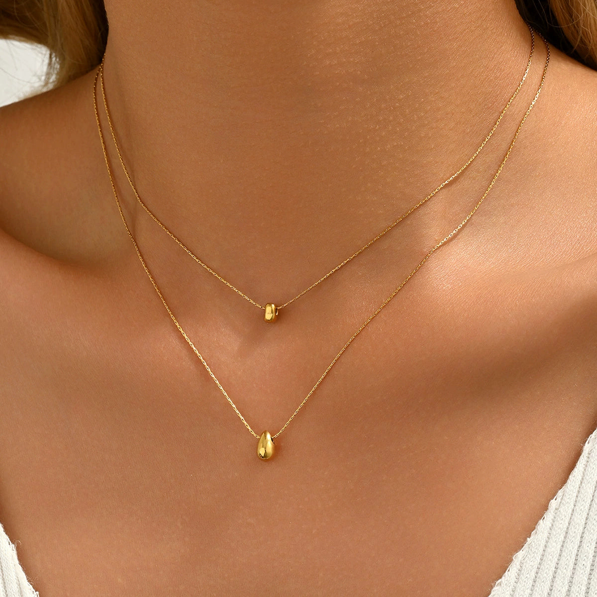 A person wearing two gold-plated necklaces with teardrop pendants from SKADIS Jewelry