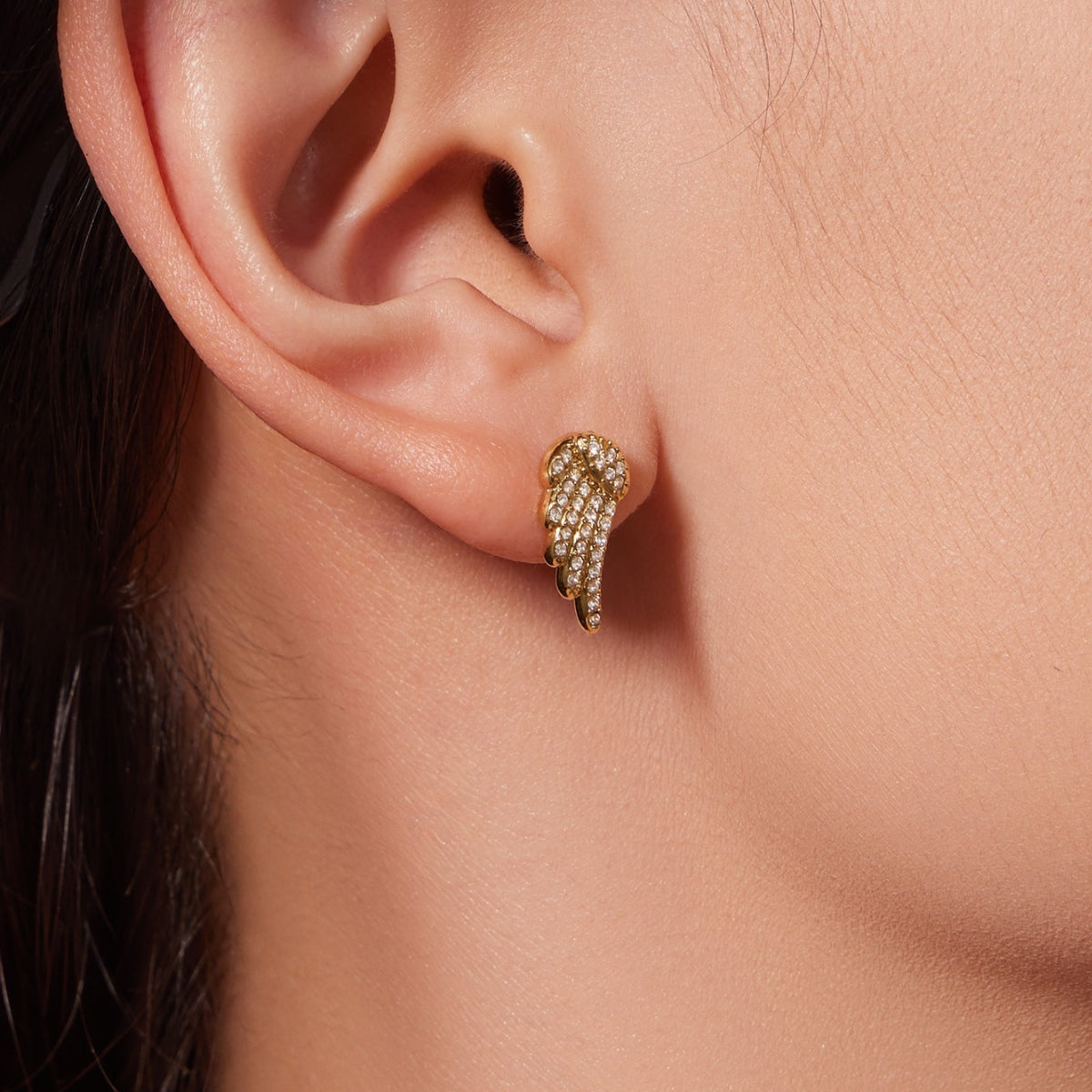A person wearing a gold angel wing earring from SKADIS Jewelry
