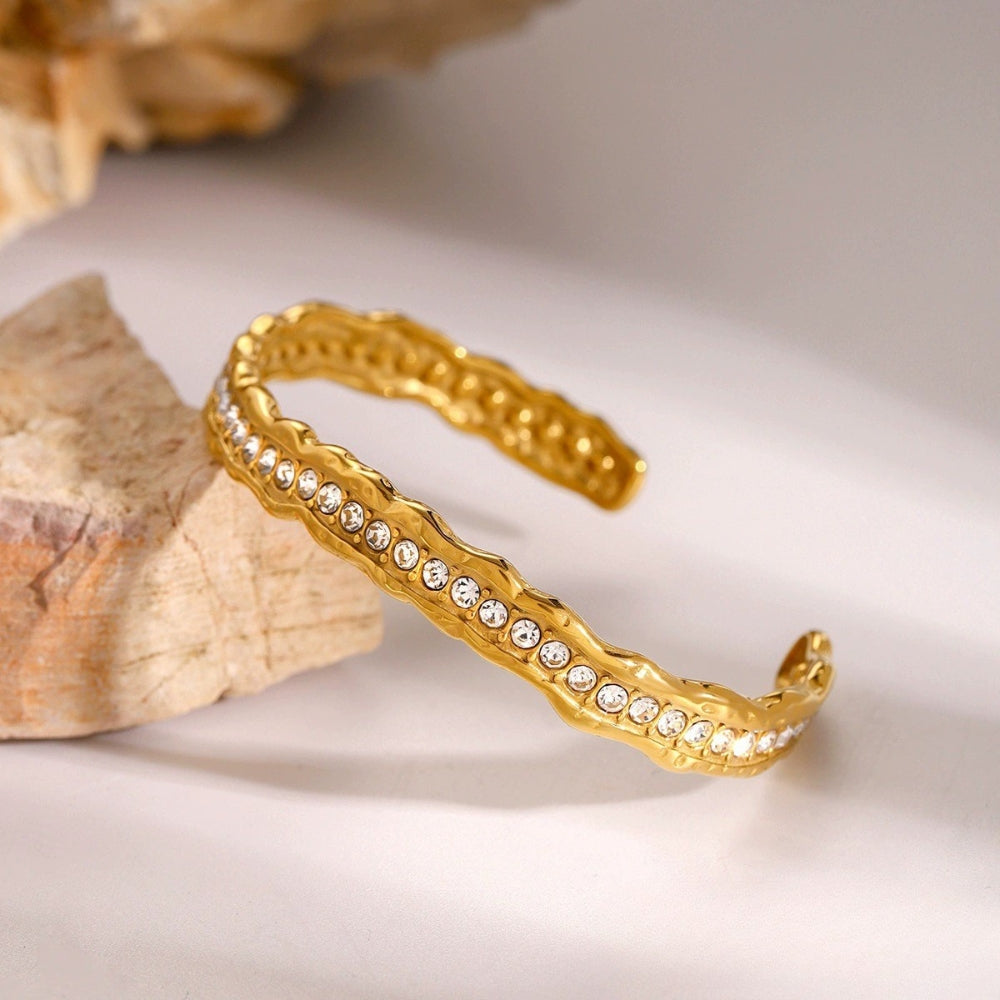 A gold open cuff bangle bracelet with a wavy textured edge from SKADIS Jewelry