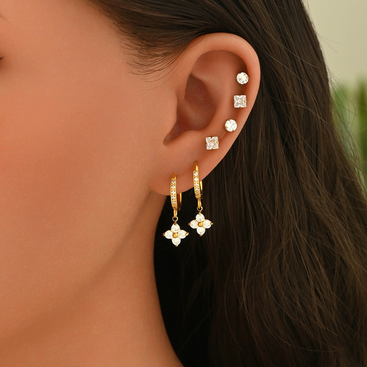 An ear wearing gold earrings with floral designs from SKADIS Jewelry