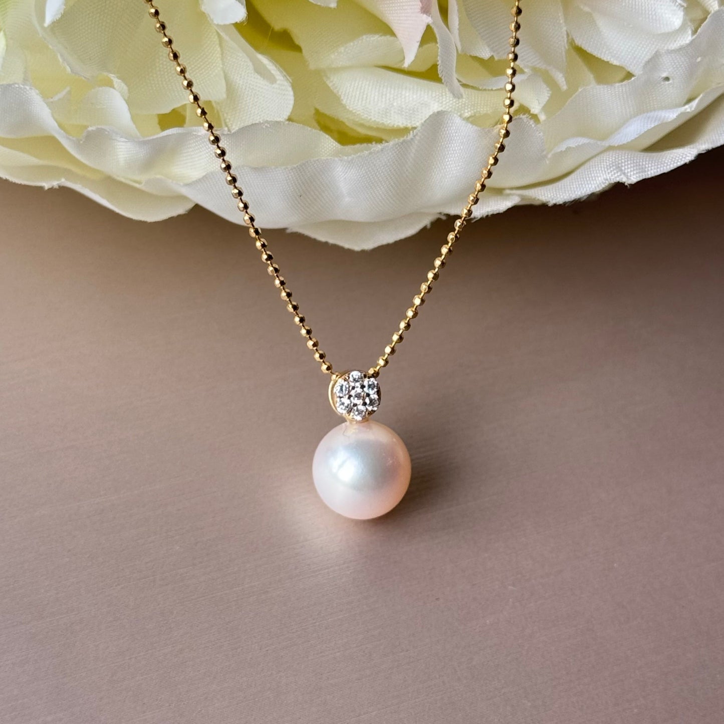 Pearl necklace with gold chain on a soft pink background.