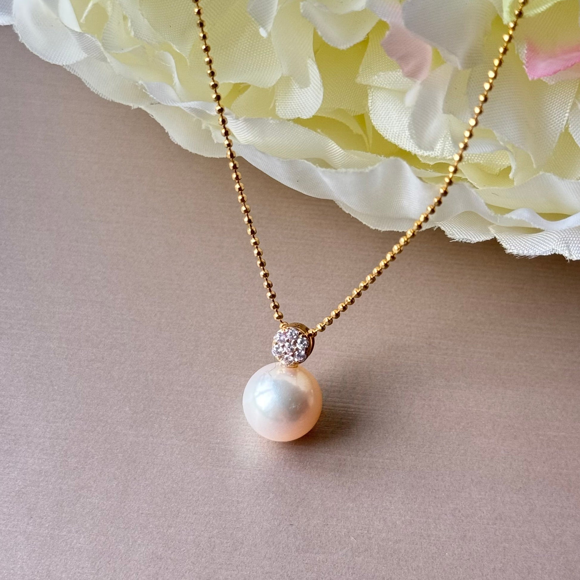 Pearl necklace with a gold chain on a light background.