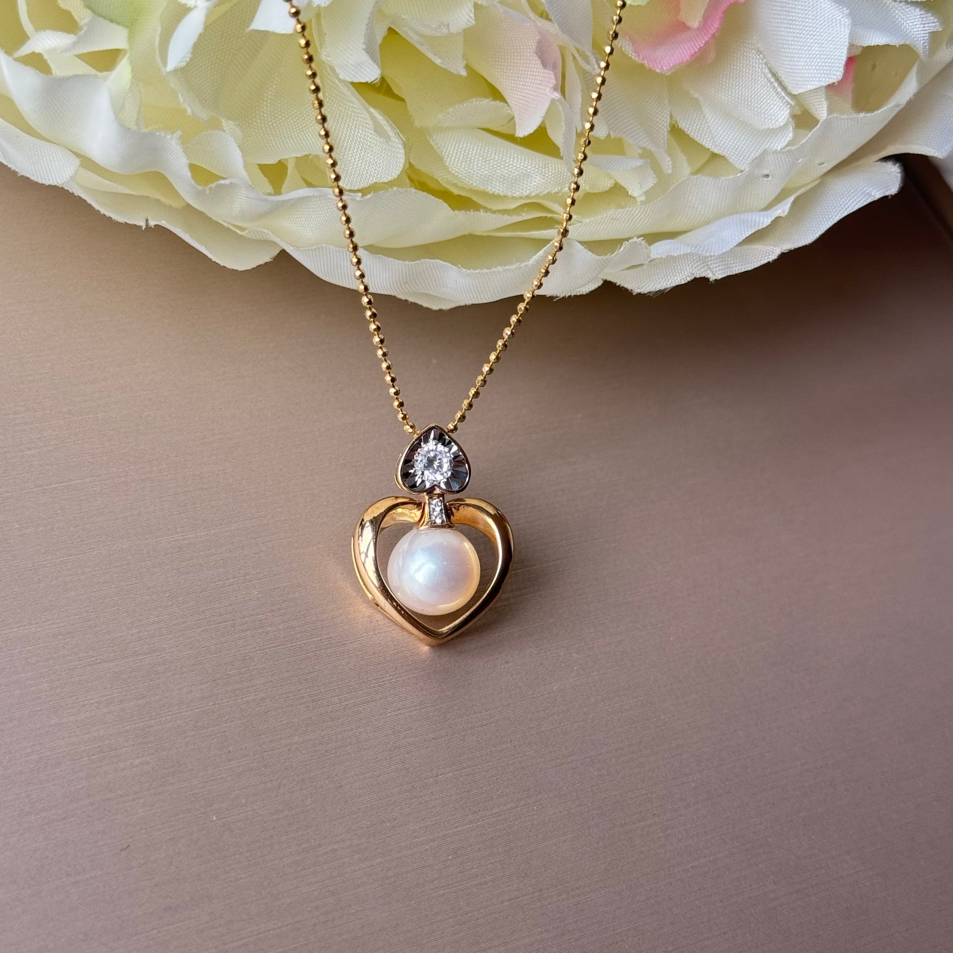 Gold necklace with a heart-shaped pendant featuring a pearl.