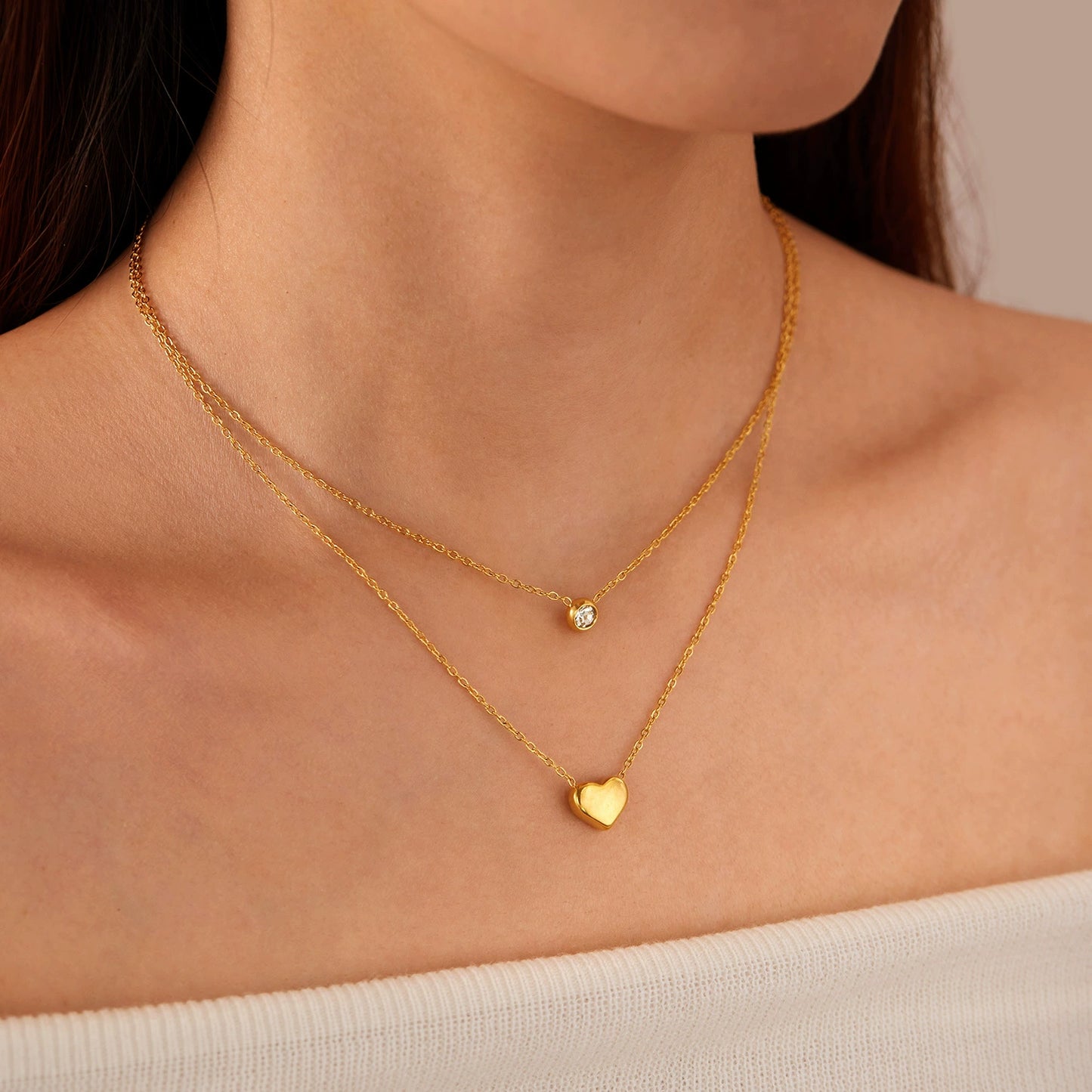 Close-up of a person wearing two gold necklaces with heart and round zirconia -SKADIS Jewelry