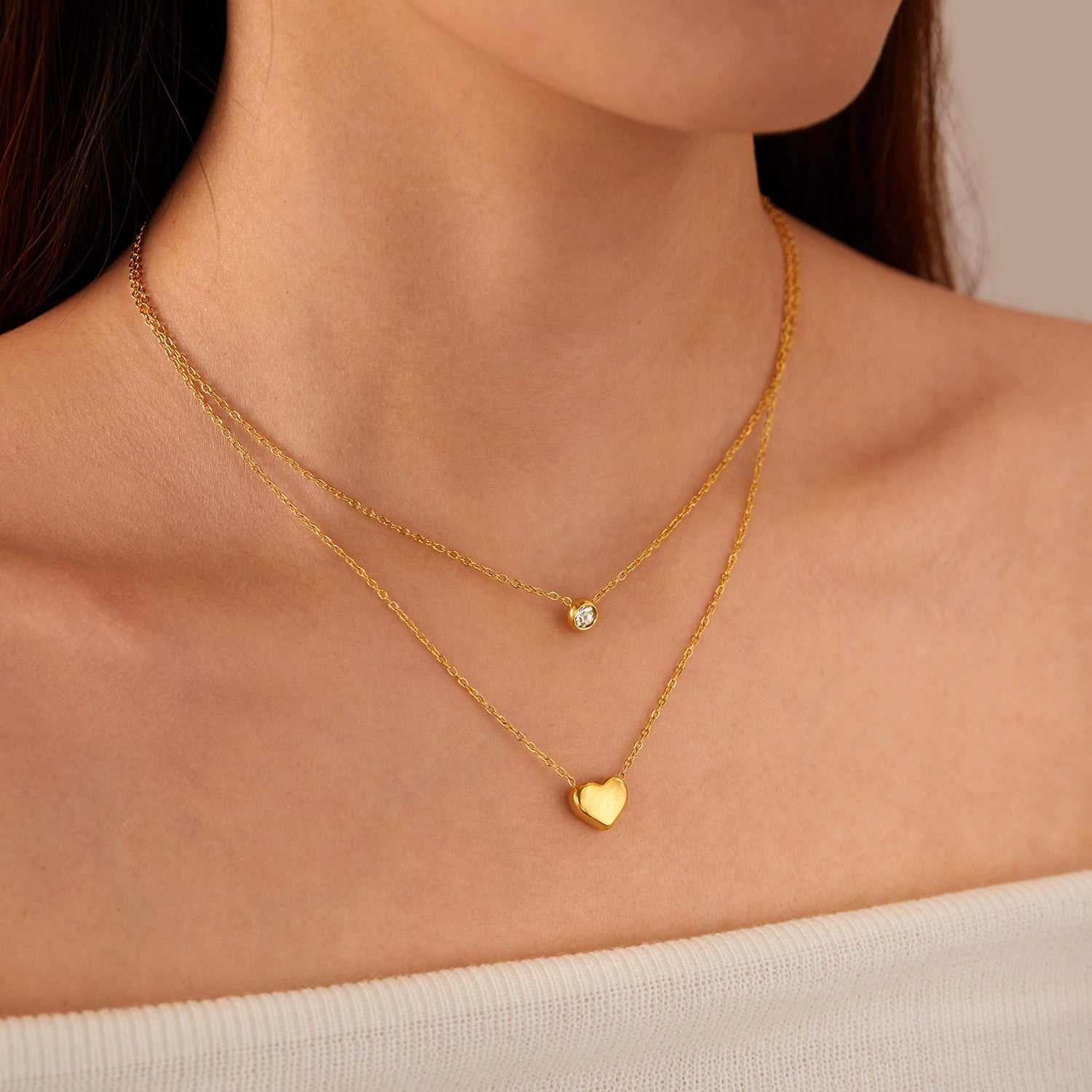 Close-up of a person wearing two gold necklaces with heart and round zirconia -SKADIS Jewelry