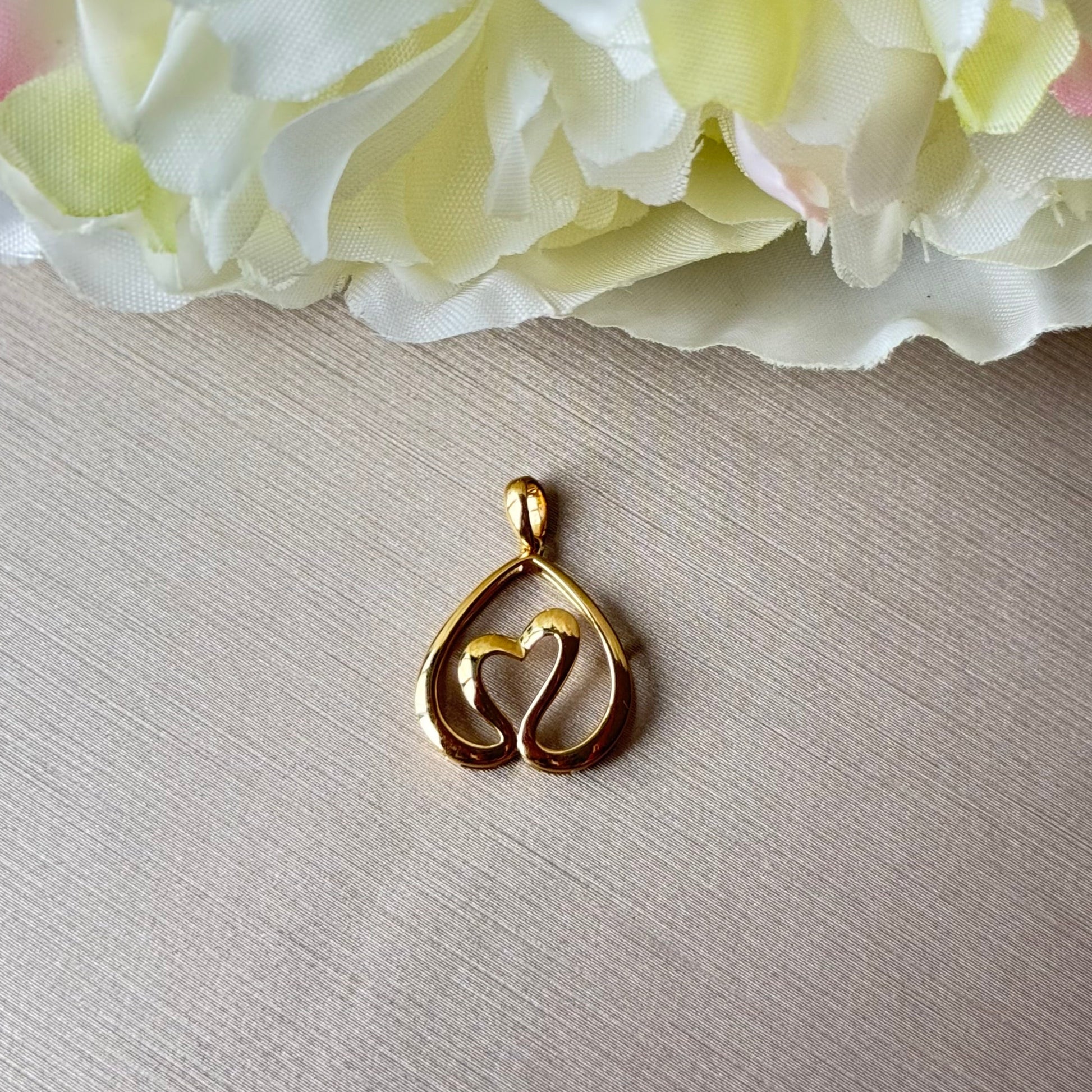 Gold pendant on a light surface with flowers in the background.