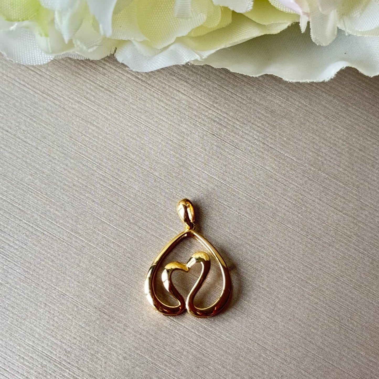 Gold pendant on a light gray surface with flowers in the background.