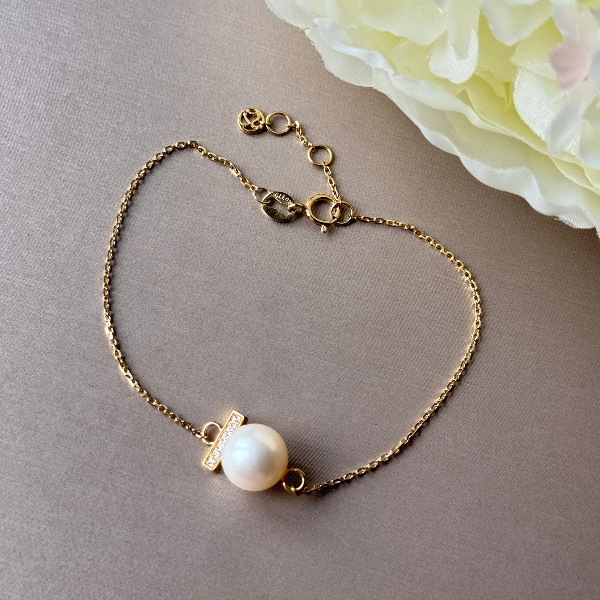 Gold bracelet with a pearl on a gray surface with a flower in the corner.