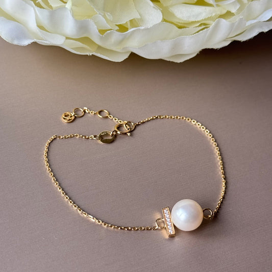 Gold bracelet with a pearl bead on a neutral background.