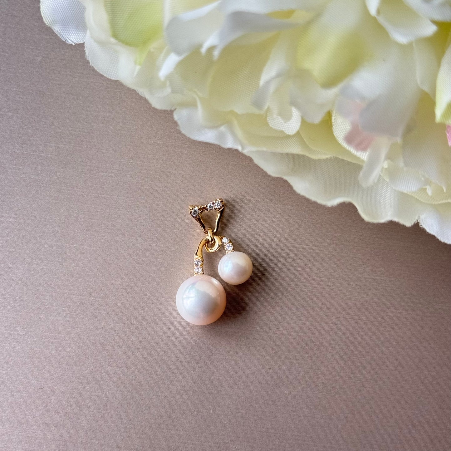 Pearl pendant with gold setting on a gray surface with a white flower in the background.