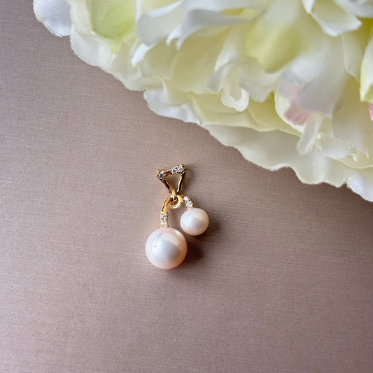 Pearl pendant with gold setting on a gray surface with a white flower in the background.