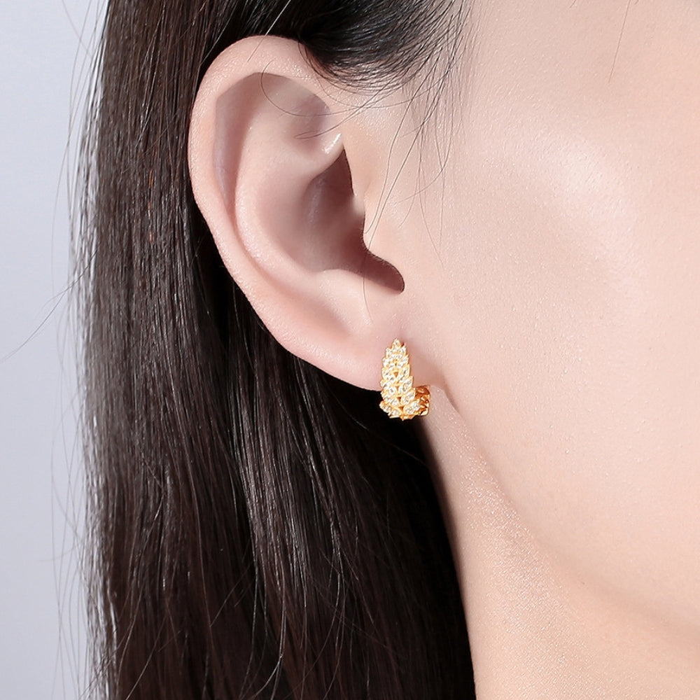Gold earrings worn by a person with dark hair against a neutral background.
