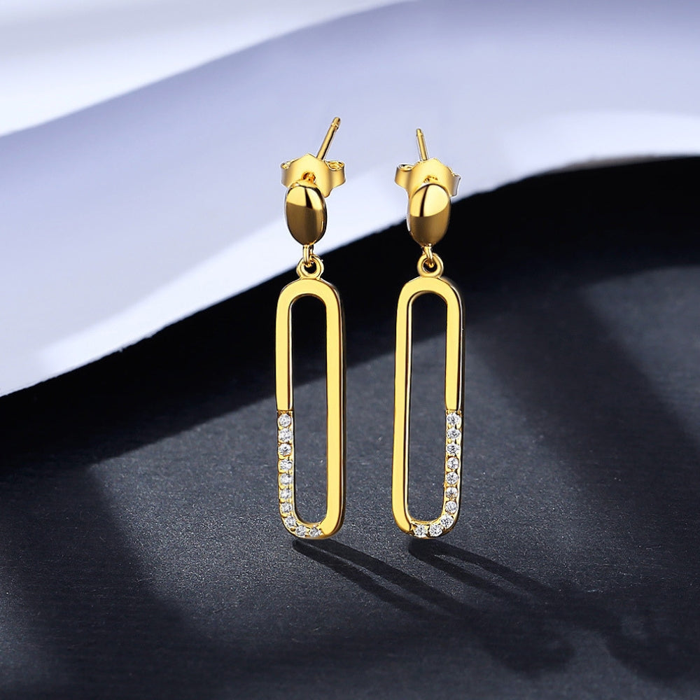 Gold earrings with small zirconias on a dark surface.