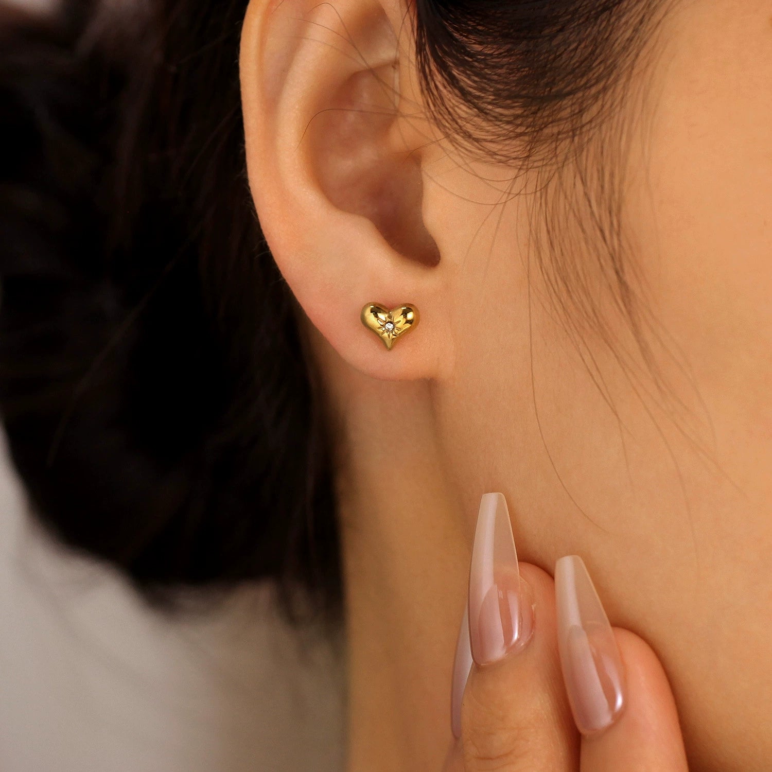 A person wearing a gold heart-shaped earring from SKADIS Jewelry