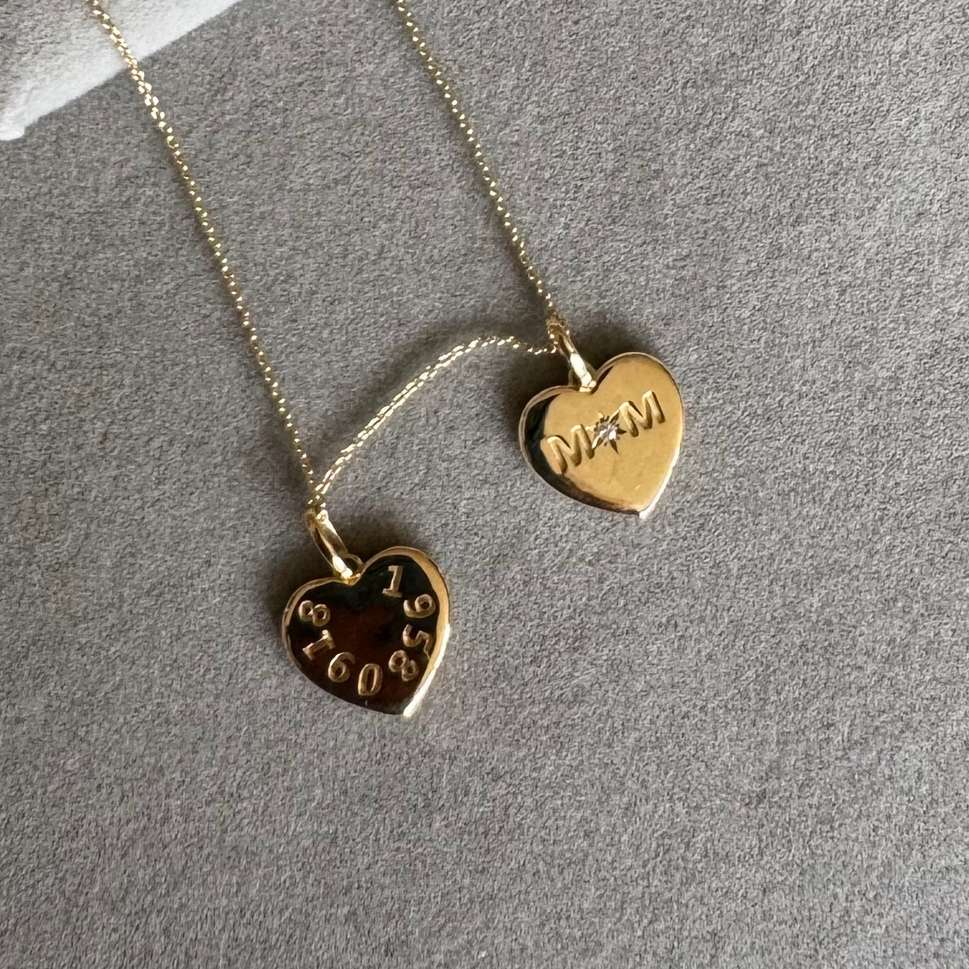 Two gold heart-shaped pendant necklaces on a textured gray background from SKADIS Jewelry