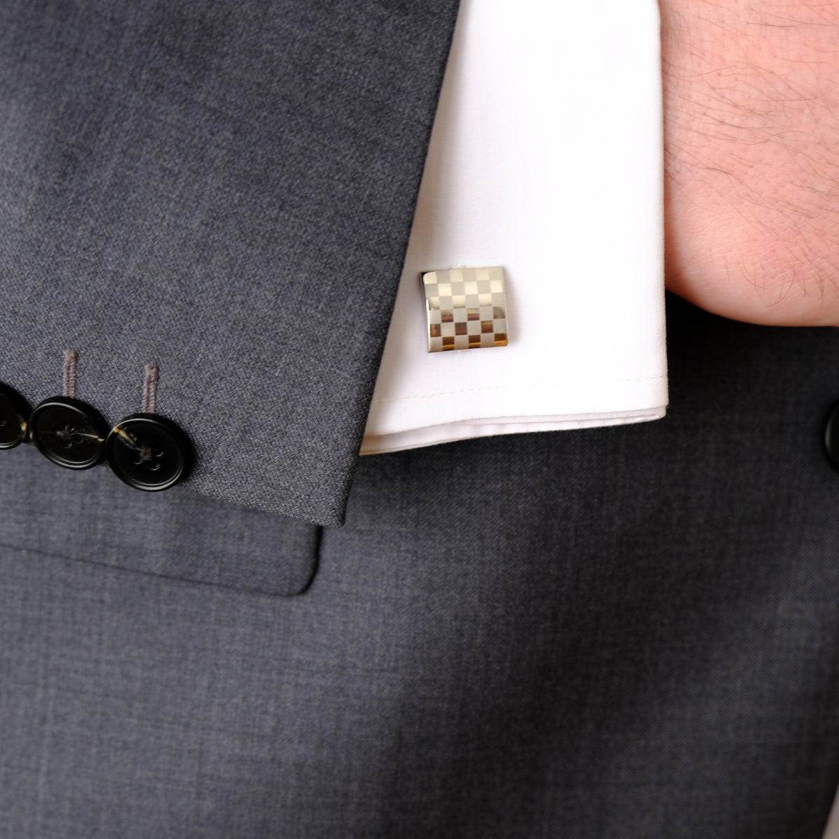 Close-up of a gray suit jacket with a checkered cufflink SKADIS Jewelry