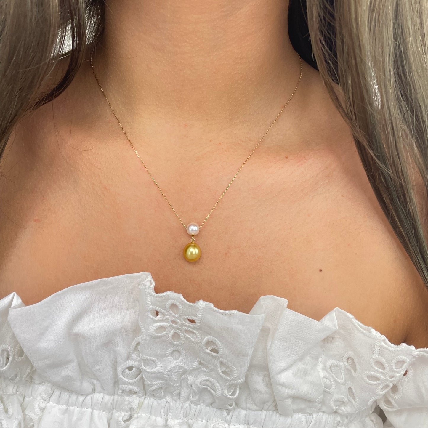 Close-up of a 18k gold necklace with Akoya and Southsea gold pearl on a model wearing a white top.