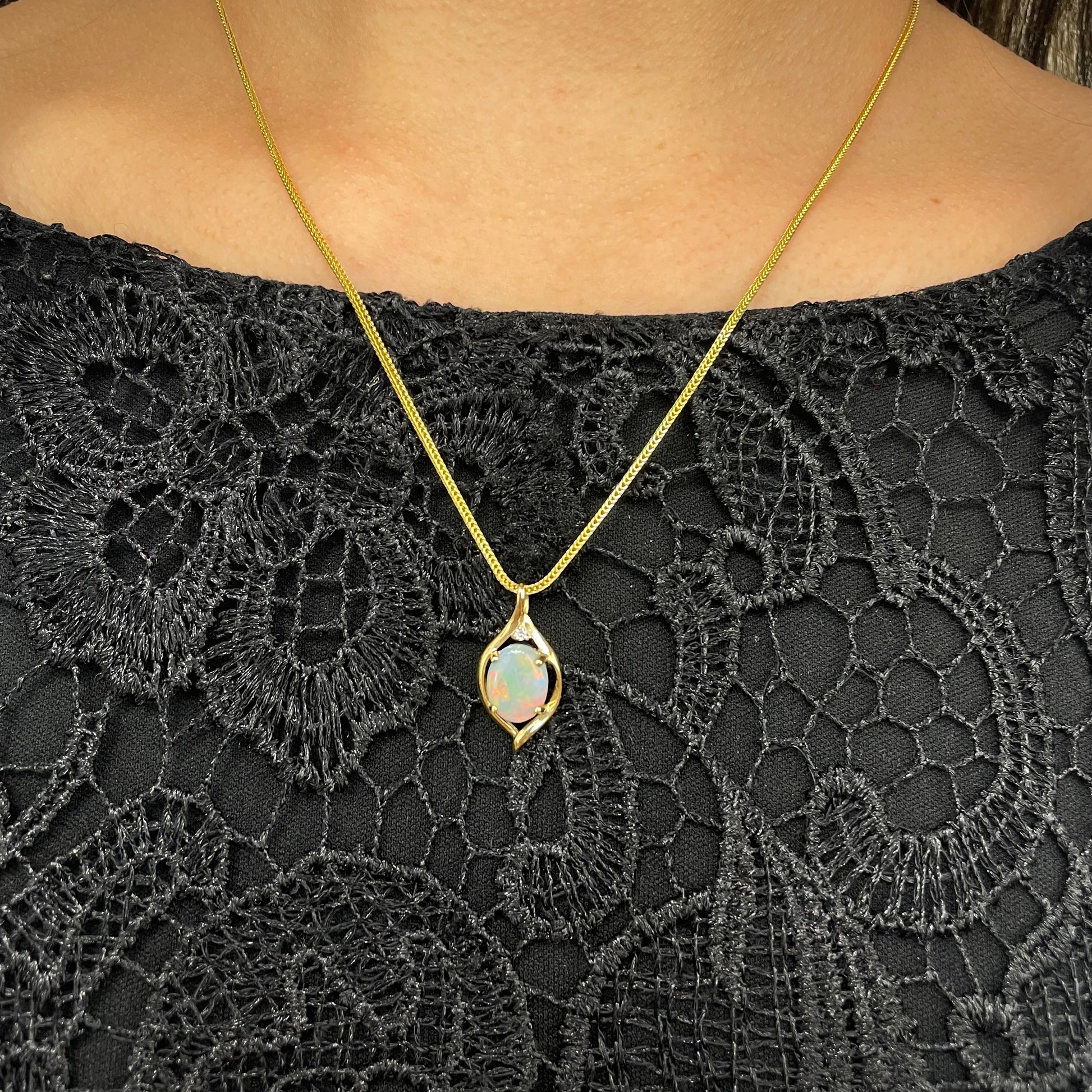 Australian natural opal pendant in 14k gold and diamond on a background of black clothes