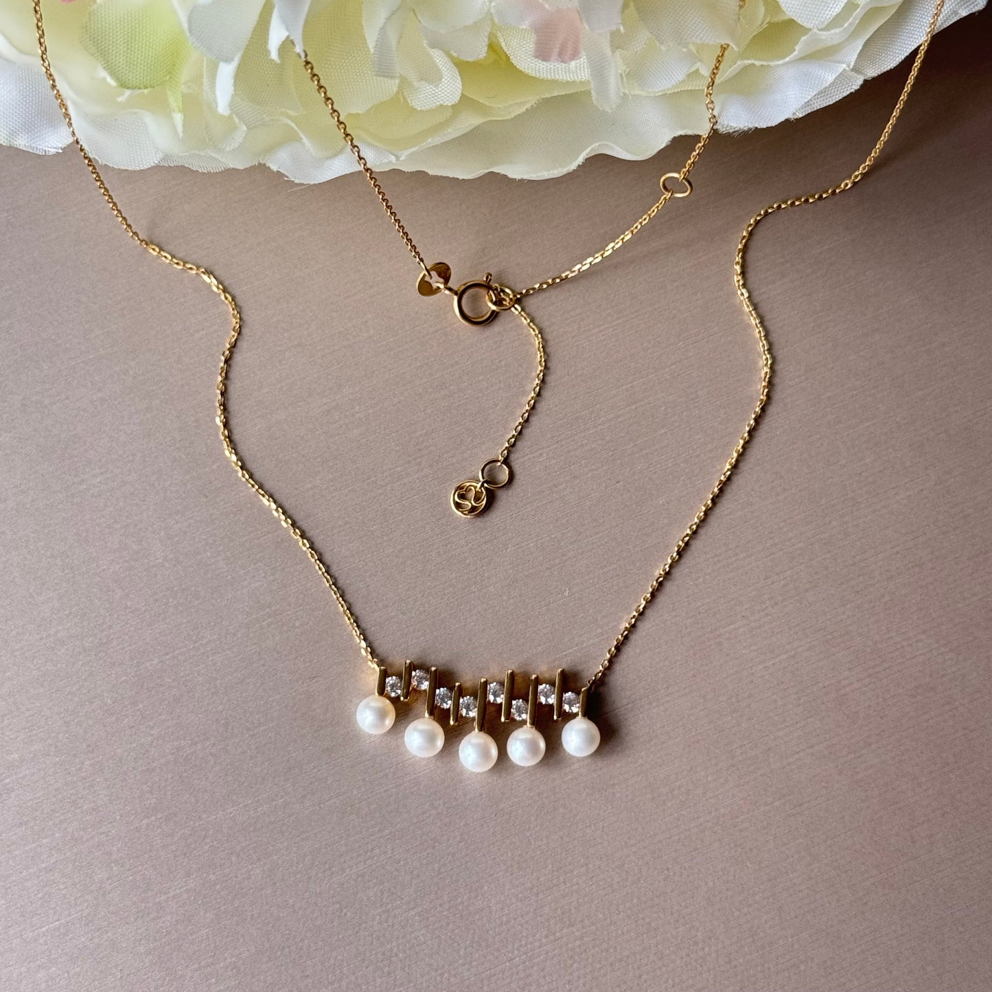 Gold necklace with pearl drops on a beige background.