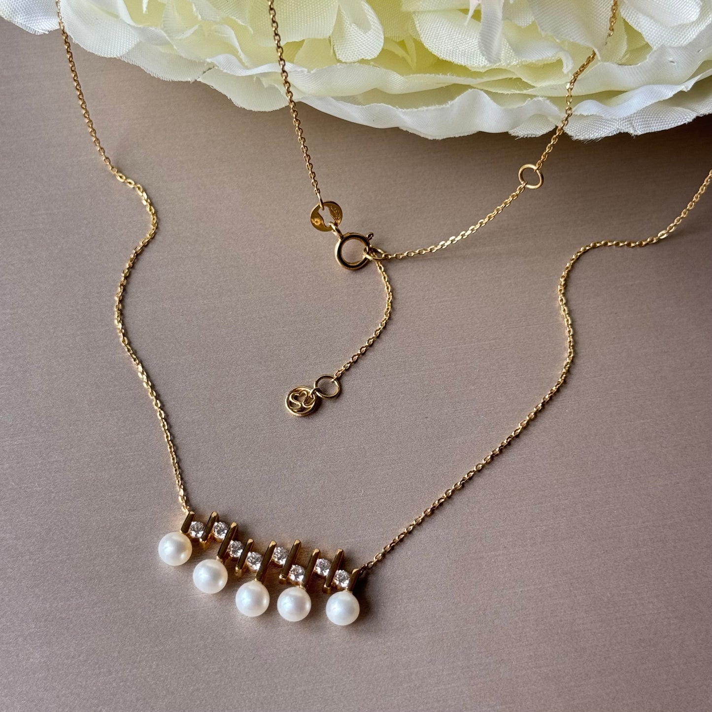Gold necklace with pearls on a gray surface with flowers in the background.
