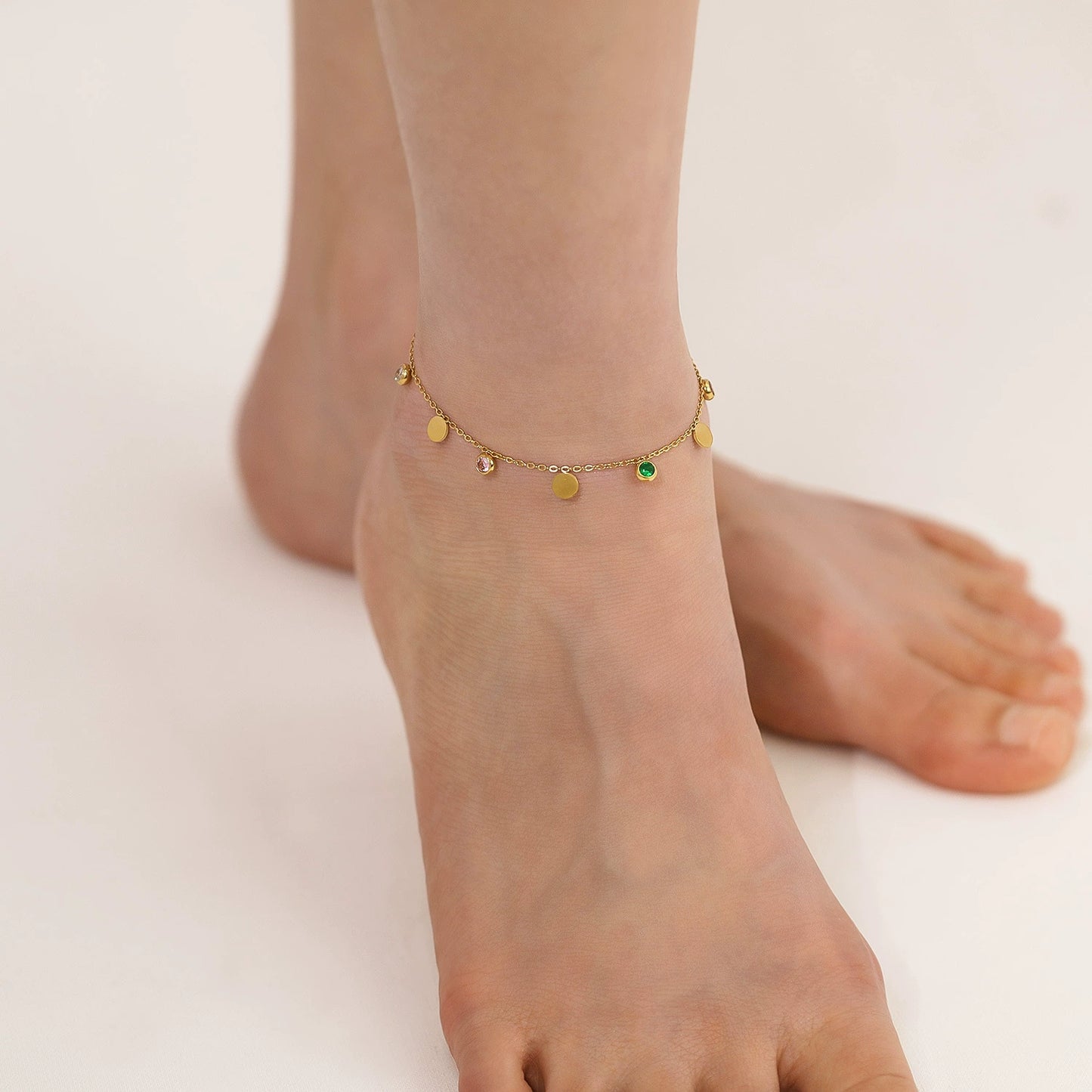 Gold-plated anklet with green gemstone on a foot from SKADIS Jewelry