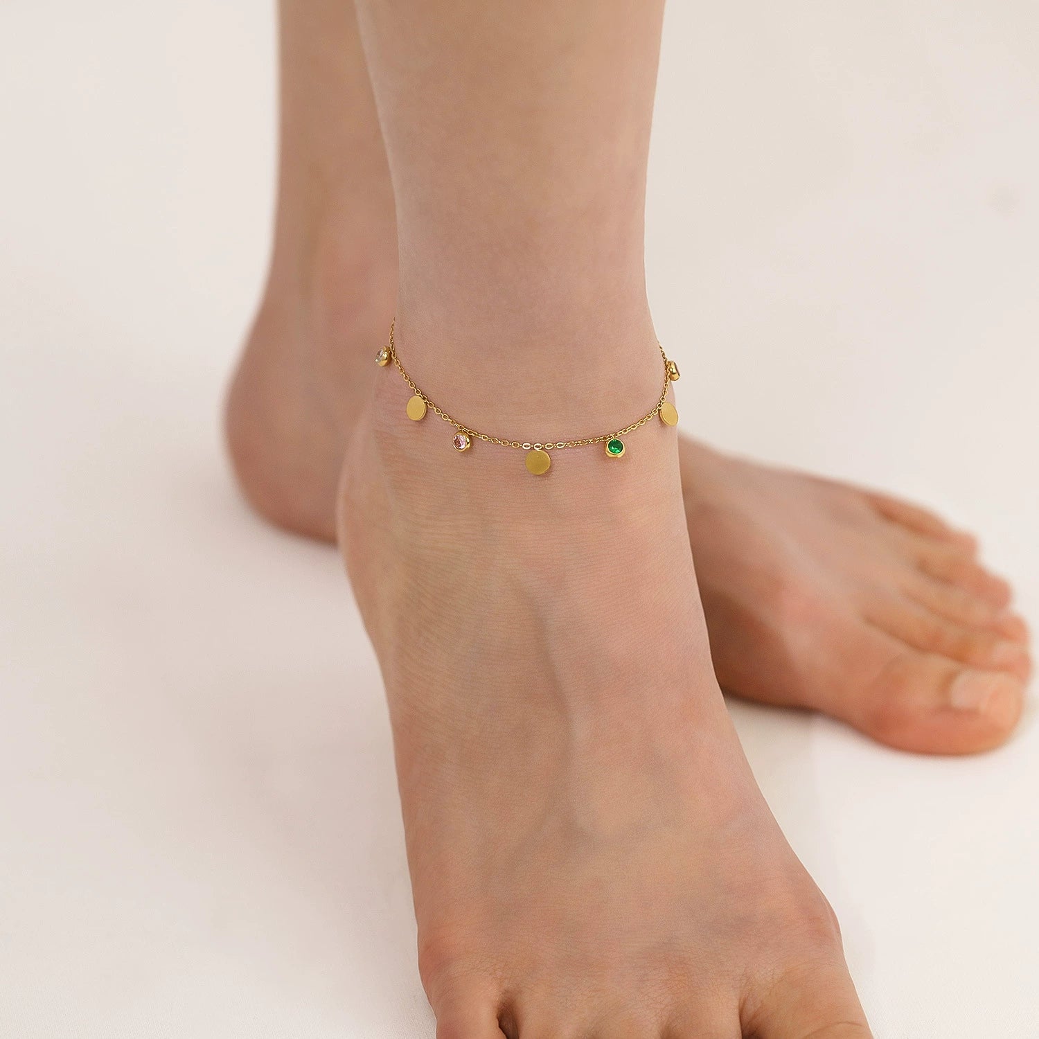 Gold-plated anklet with green gemstone on a foot from SKADIS Jewelry