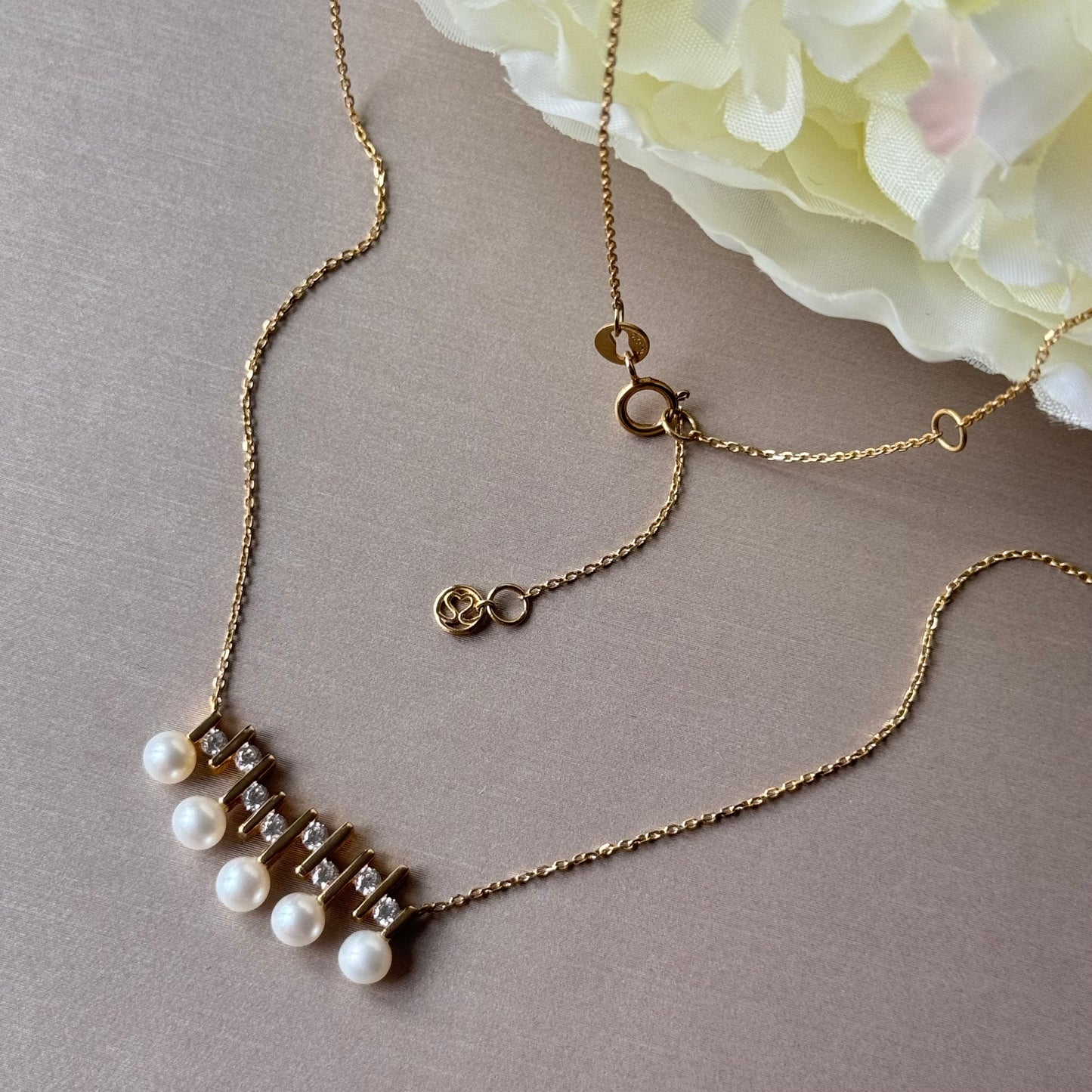 Gold necklace with pearls on a gray surface with flowers in the background.