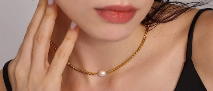 A close-up of a model wearing a delicate gold chain necklace with a single white pearl pendant from SKADIS Jewelry.