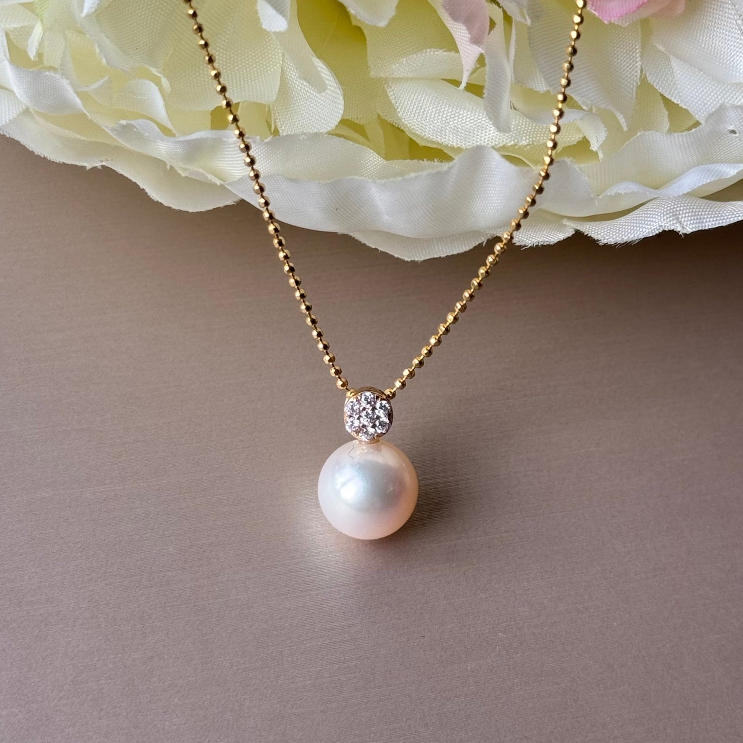 Pearl necklace with zirconias on a gray surface with white flowers in the background.